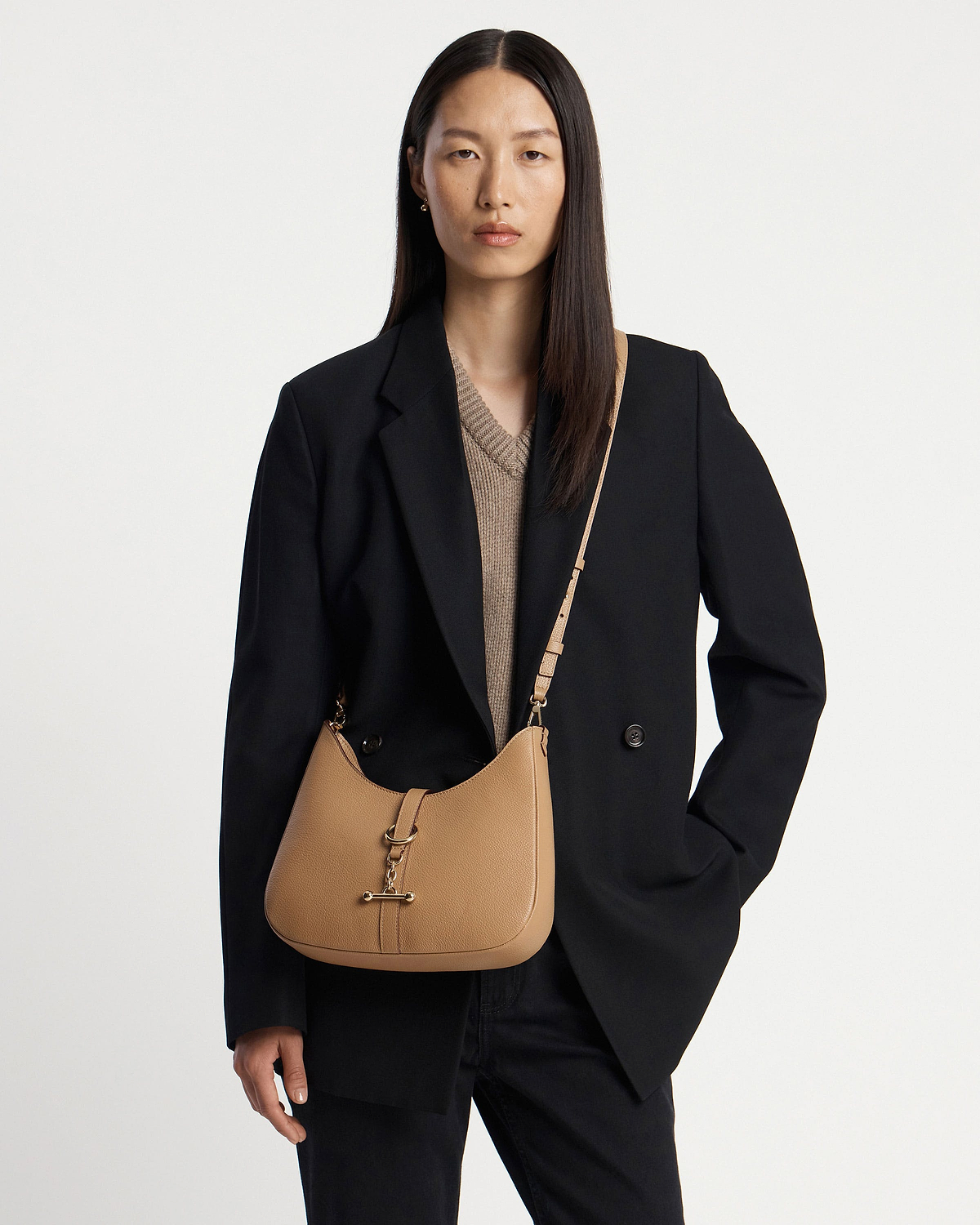 Model wearing a caramel kite sling bag with gold hardware and black blazer.