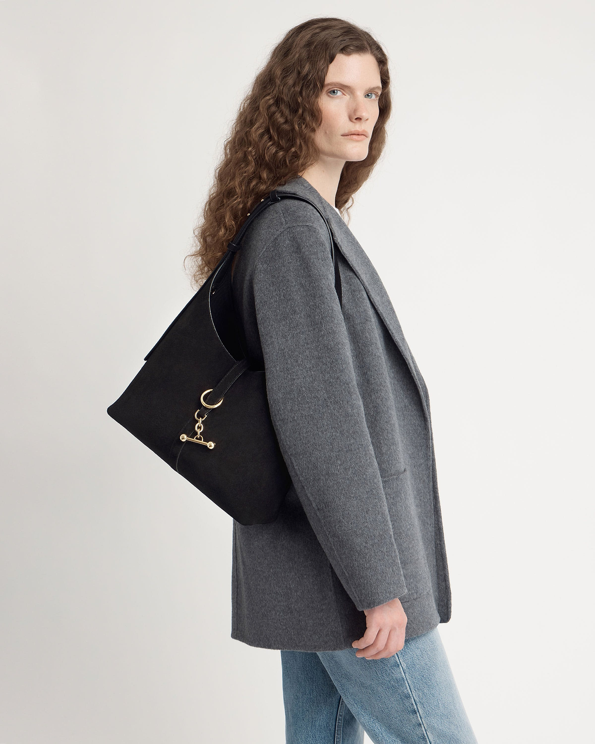 Model in grey coat wearing black suede hobo bag with gold hardware.