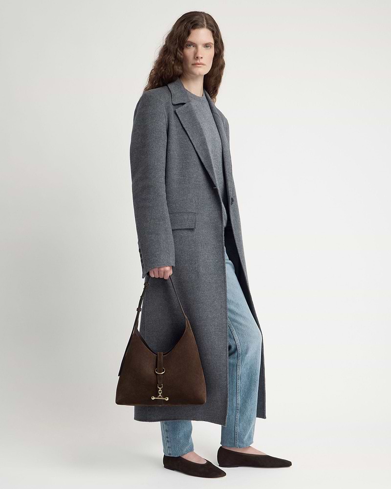 Model wearing grey coat and jeans holding chocolate suede Kite Hobo bag.