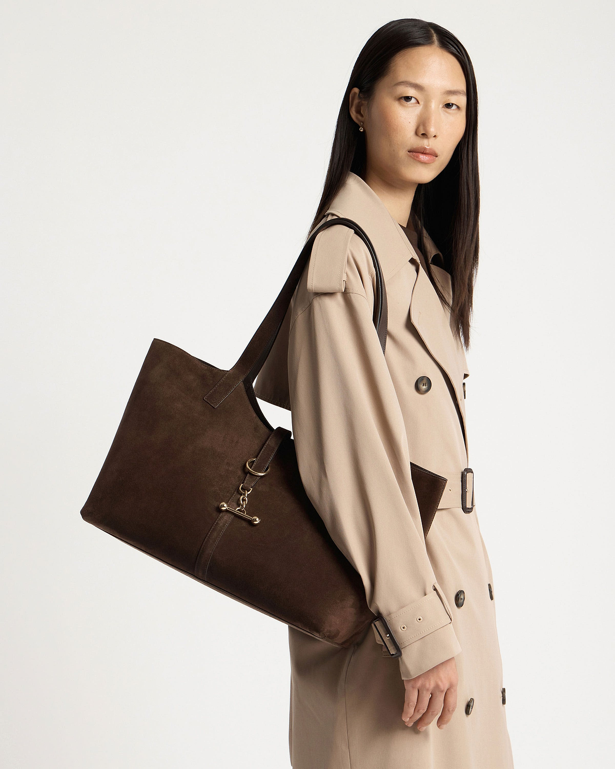 Woman wearing a beige trench coat carrying a chocolate suede Kite tote.