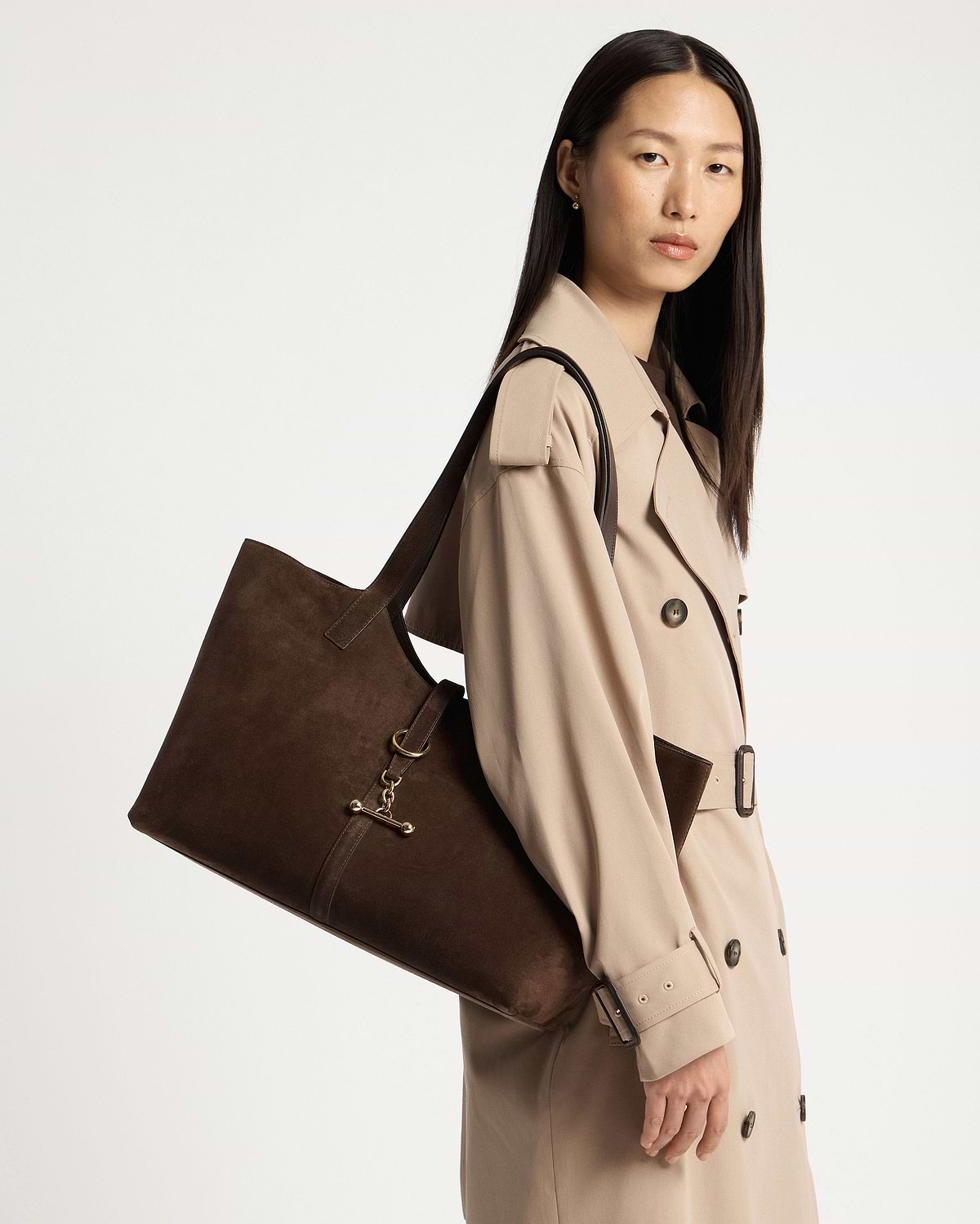 Woman wearing a beige trench coat carrying a chocolate suede Kite tote.