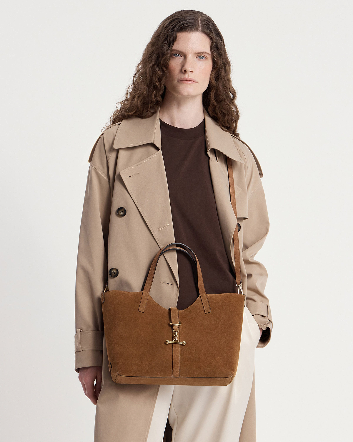 Model wearing a beige trench coat holding a tan suede Kite Tote Midi bag.
