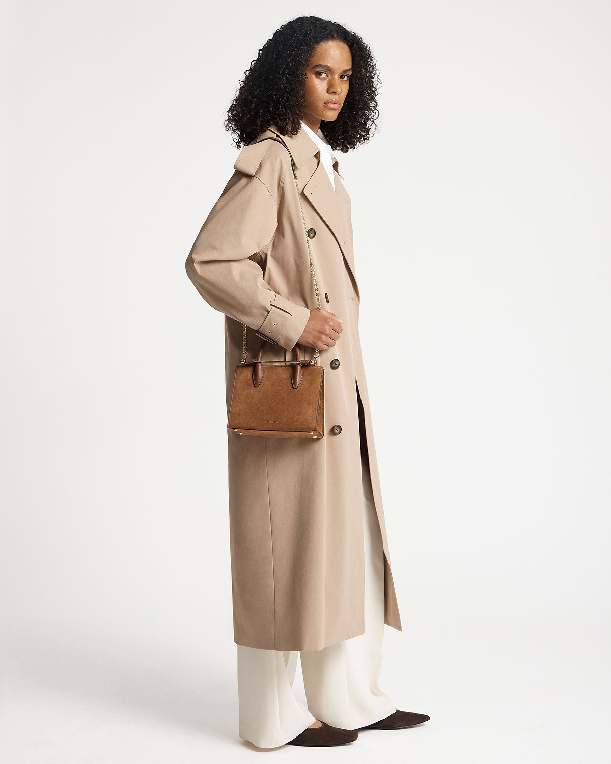 Model wearing tan suede mini tote with chain strap and top handles.