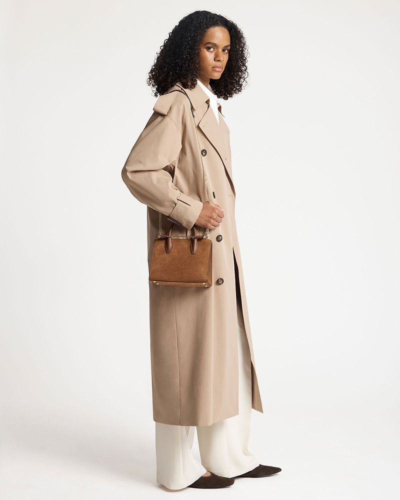Model wearing tan suede mini tote with chain strap and top handles.