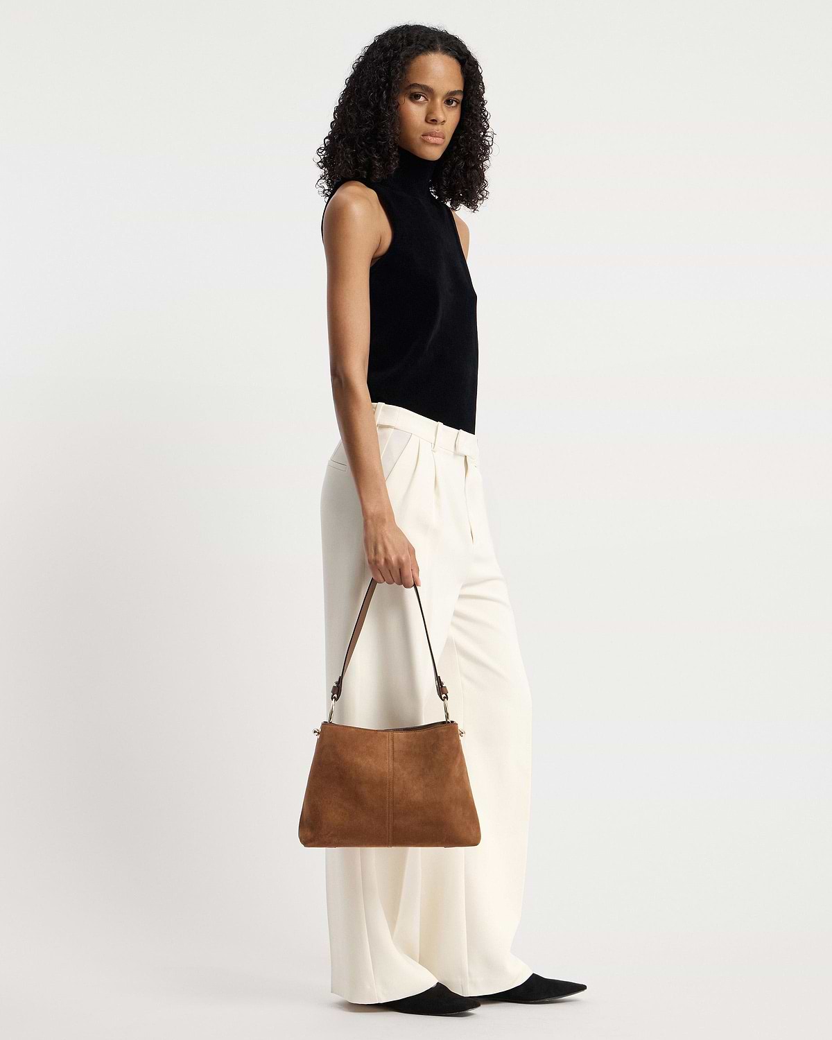 Model holding a tan suede hobo bag by its single shoulder strap.