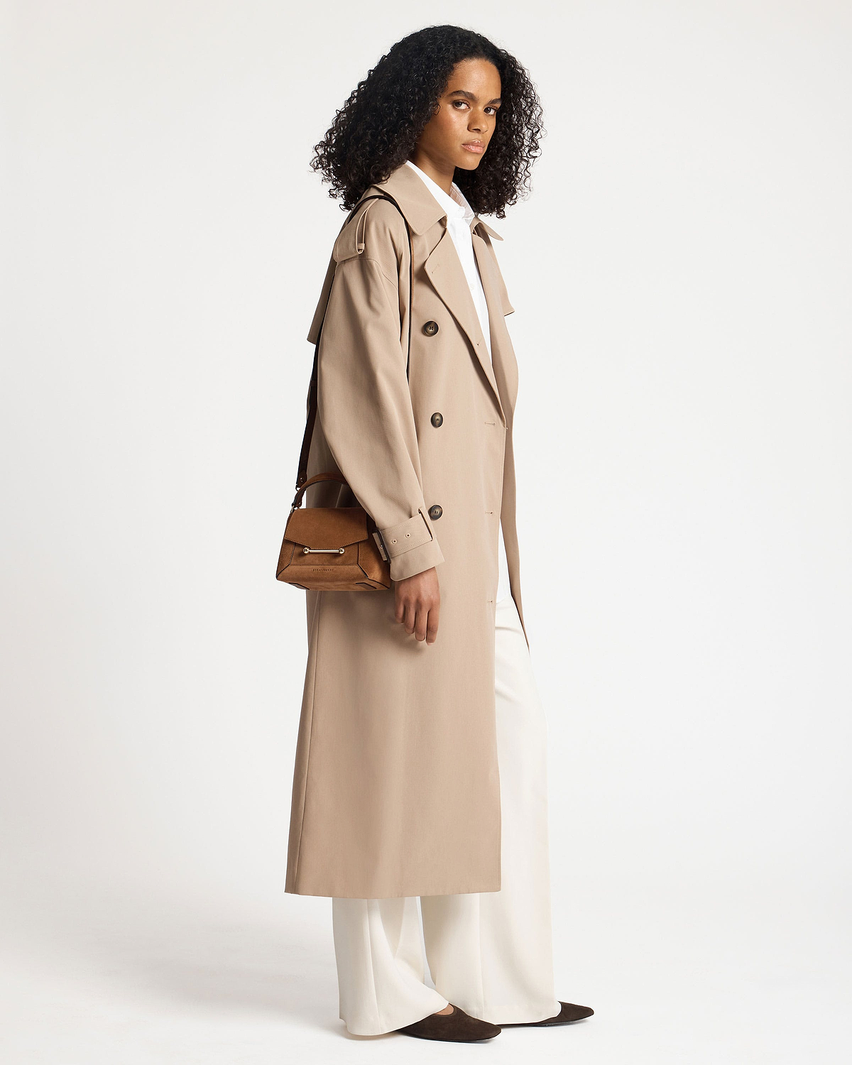 Model wearing a long beige trench and carrying a tan suede Mosaic Nano shoulder bag.