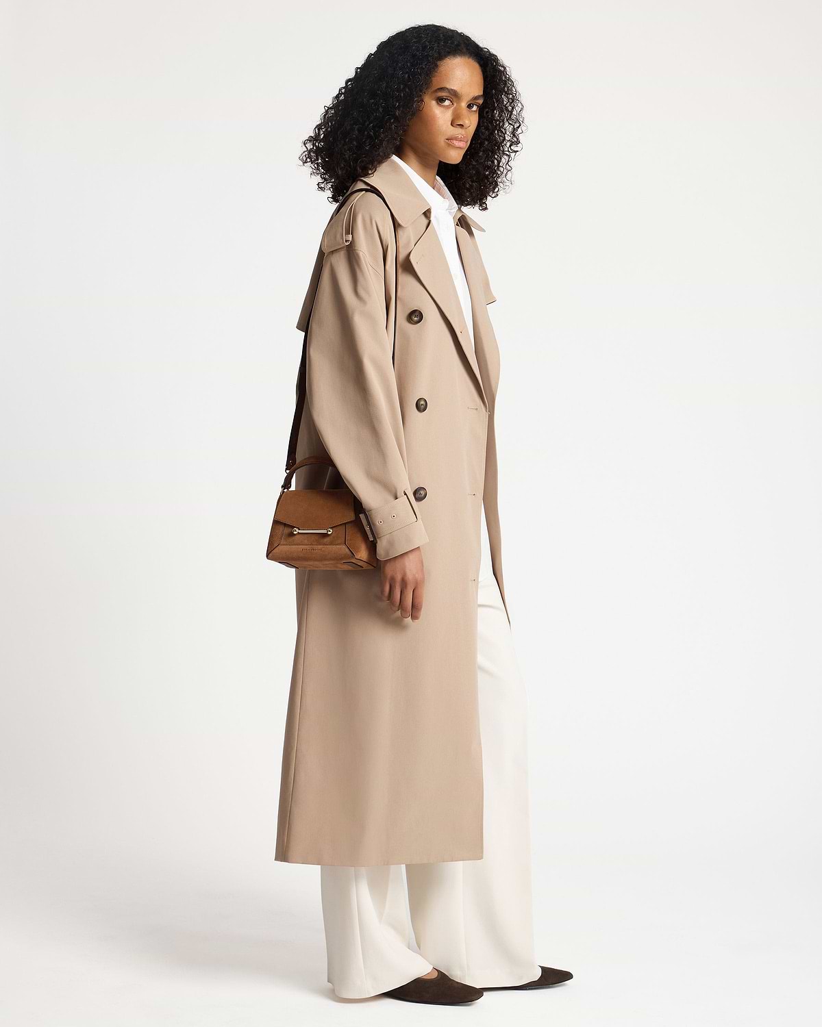 Model wearing a long beige trench and carrying a tan suede Mosaic Nano shoulder bag.