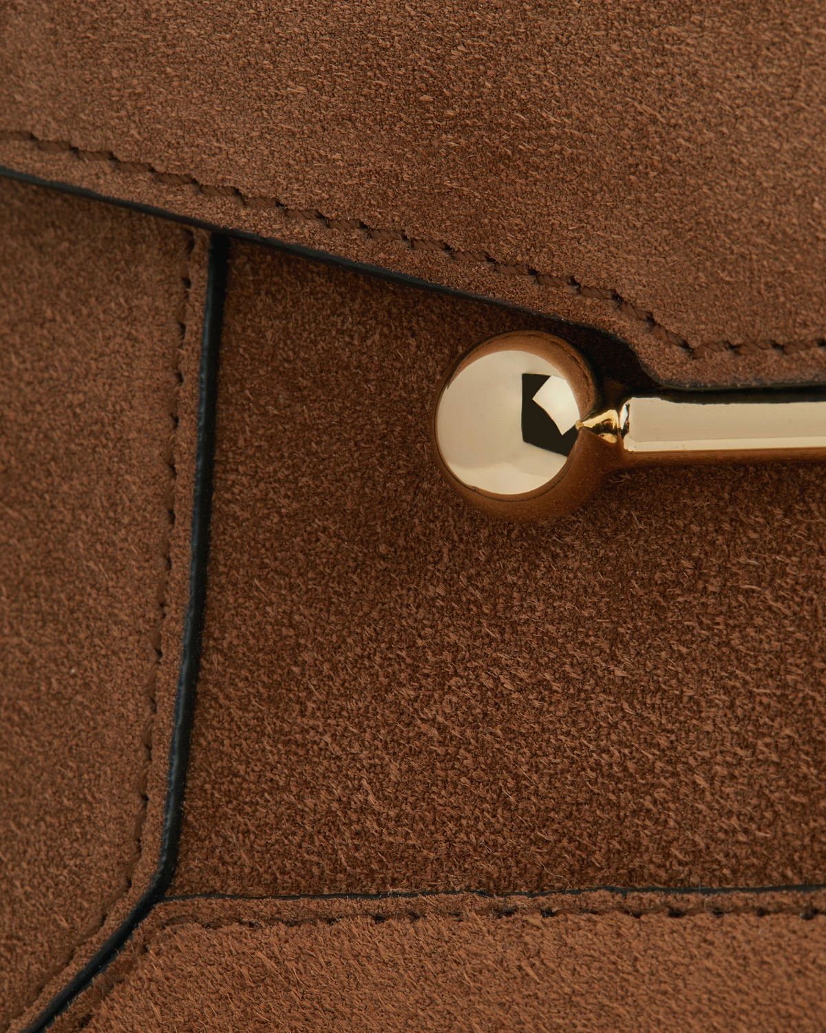 Close-up of tan suede bag panel showing gold metal stud and stitched edges.