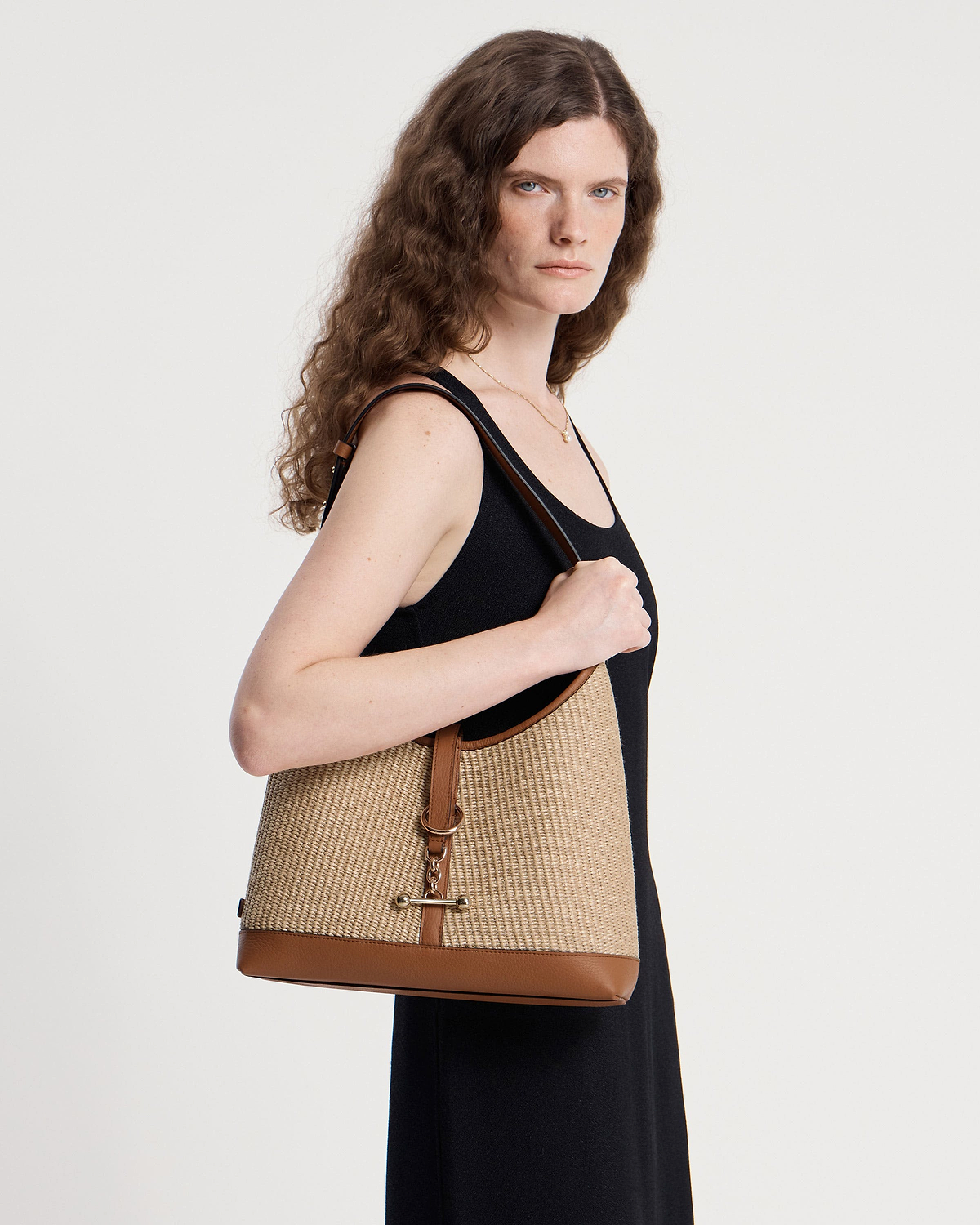 Model wearing tan natural raffia hobo bag over shoulder with leather trim.