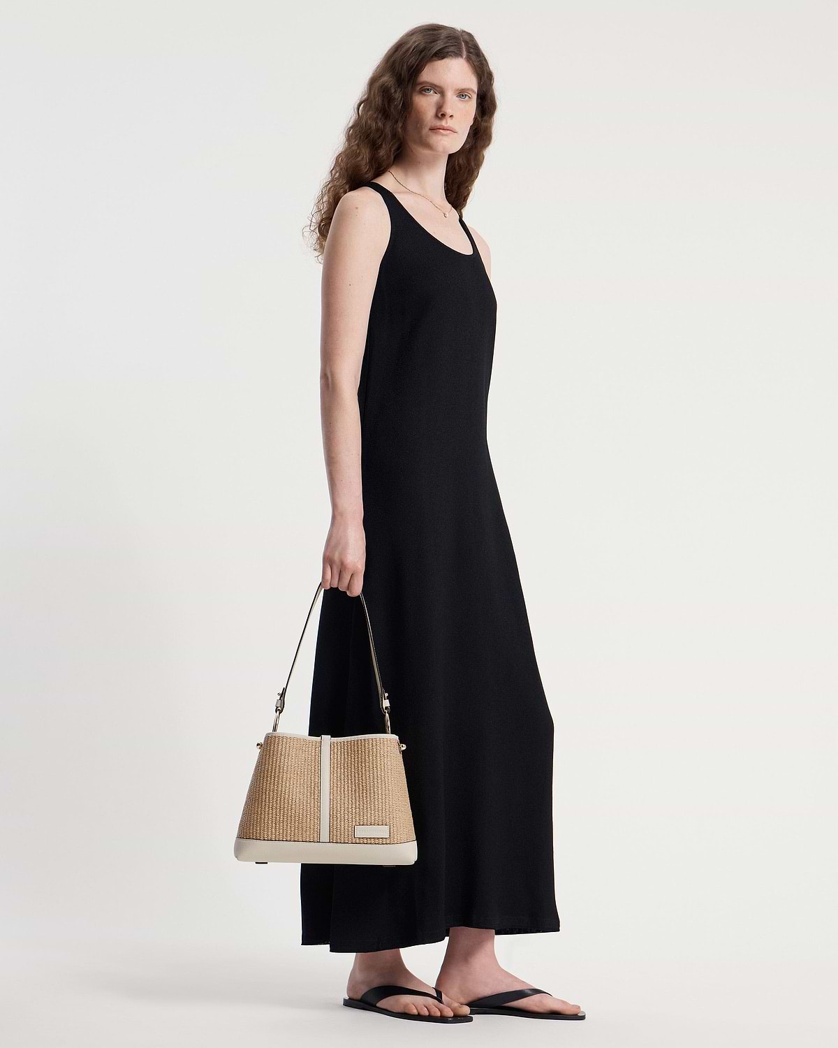 Woman in black dress holding a vanilla natural raffia hobo bag.