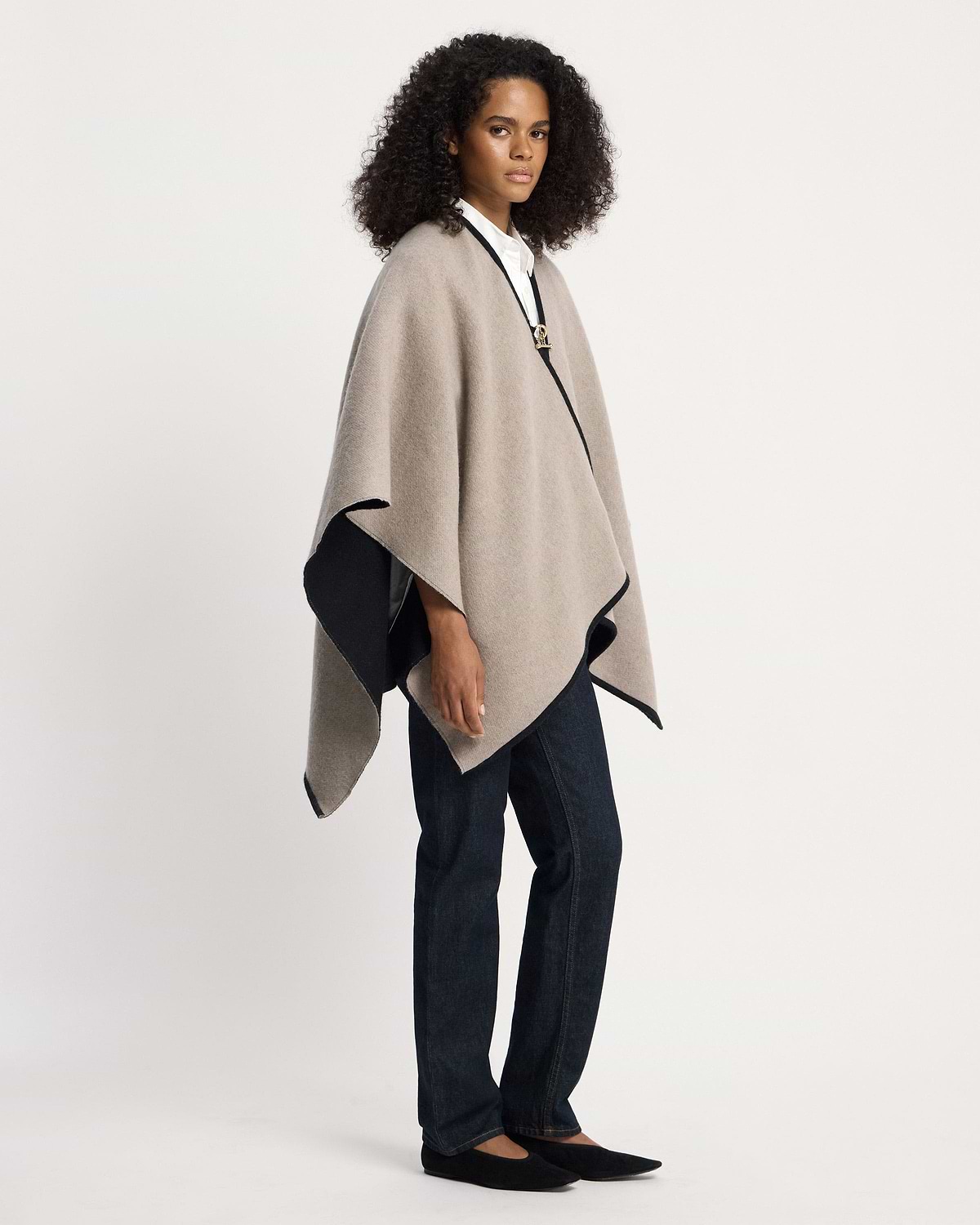 Model wearing an otter and black kite woven cape over white shirt and jeans.