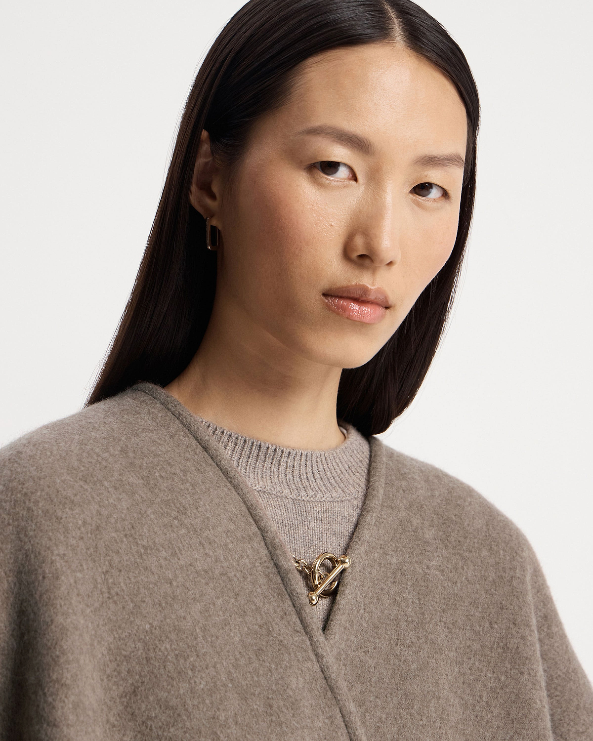 Taupe kite woven cape with gold toggle clasp worn over a knitted jumper.
