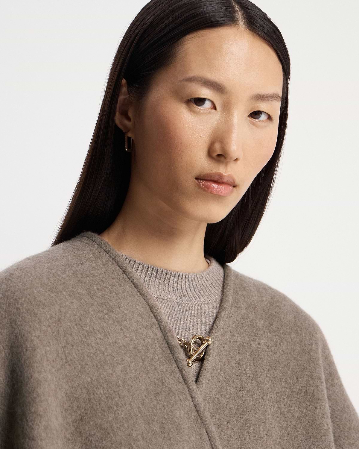 Taupe kite woven cape with gold toggle clasp worn over a knitted jumper.