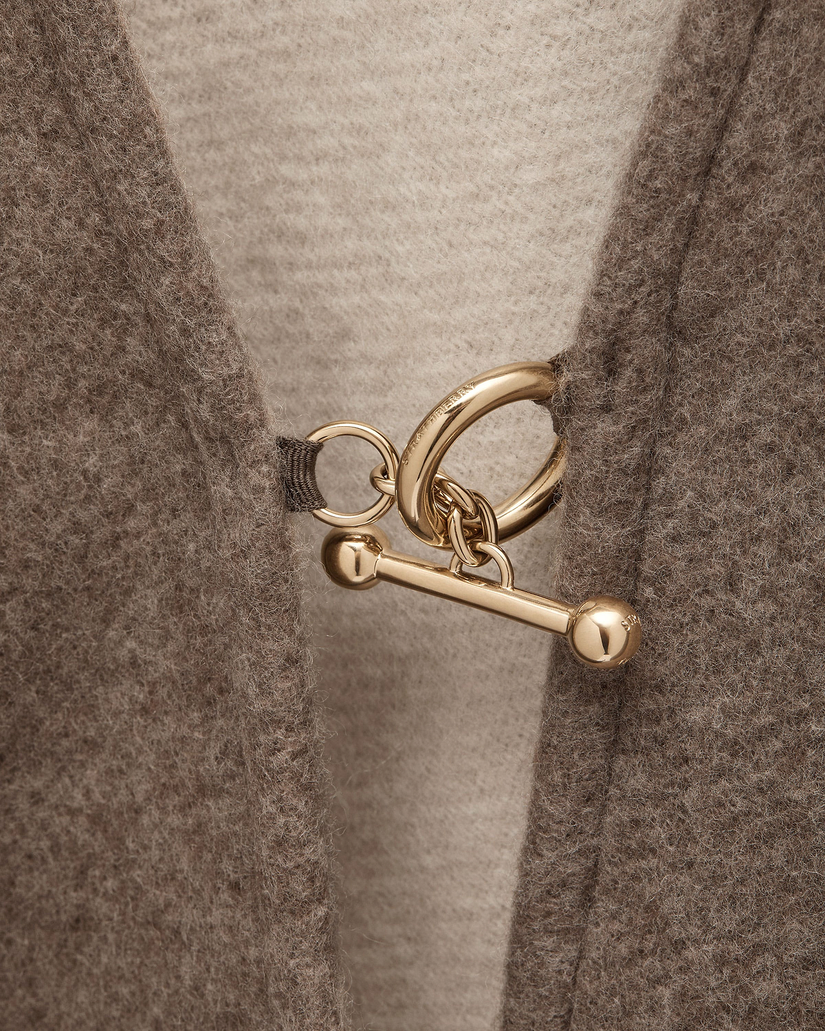 Close-up of taupe woven cape showing gold ring and toggle fastener.