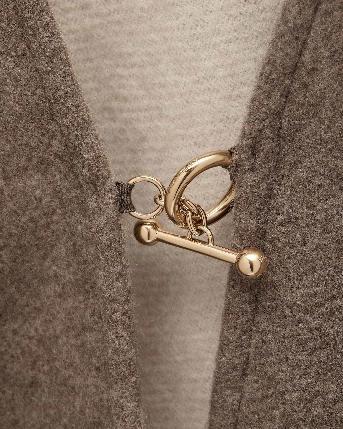 Close-up of taupe woven cape showing gold ring and toggle fastener.
