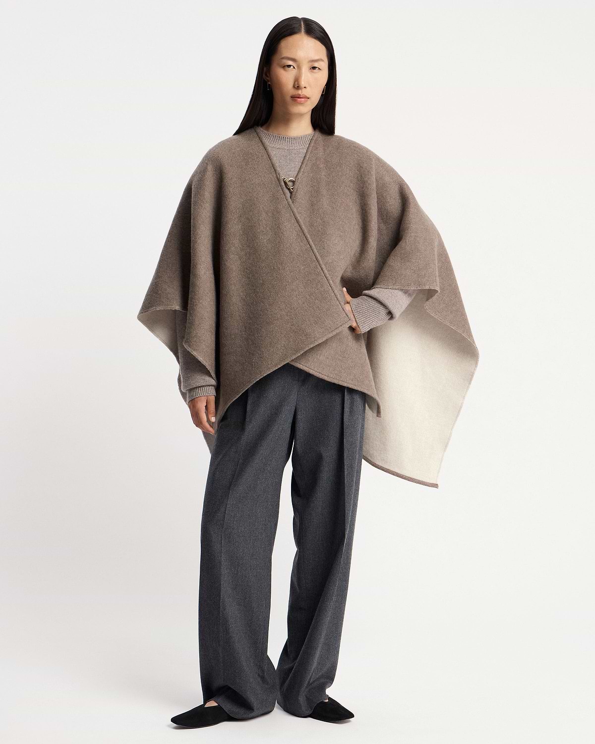 Model wearing a taupe kite woven cape over knit sweater and trousers.