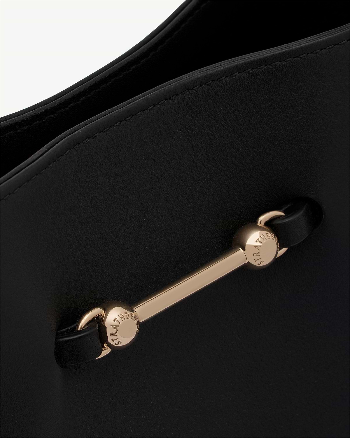 Black leather bag detail with gold Strathberry bar and stitching.