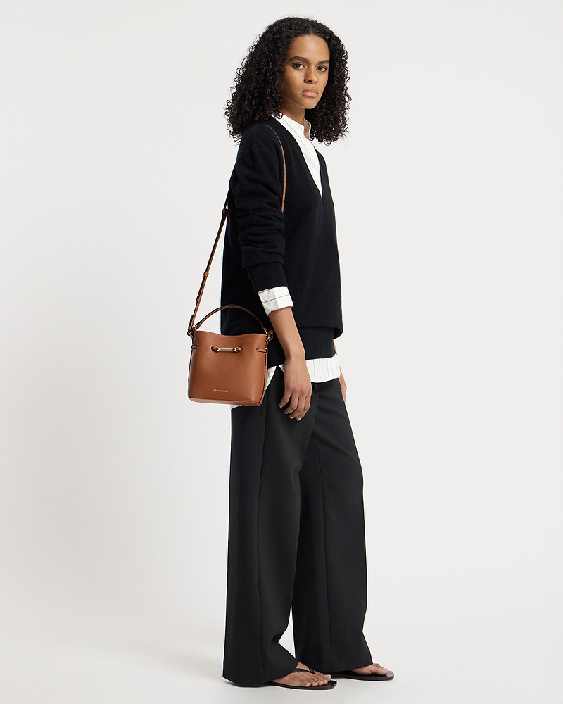 Model wearing Strathberry Corda Bucket Mini chestnut leather bag on shoulder.
