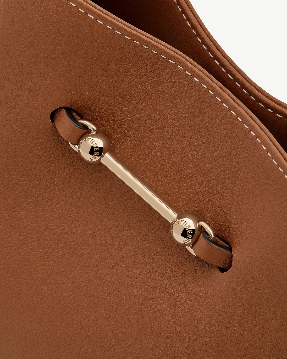 Detail of chestnut leather Strathberry bag with gold bar hardware and white stitching.