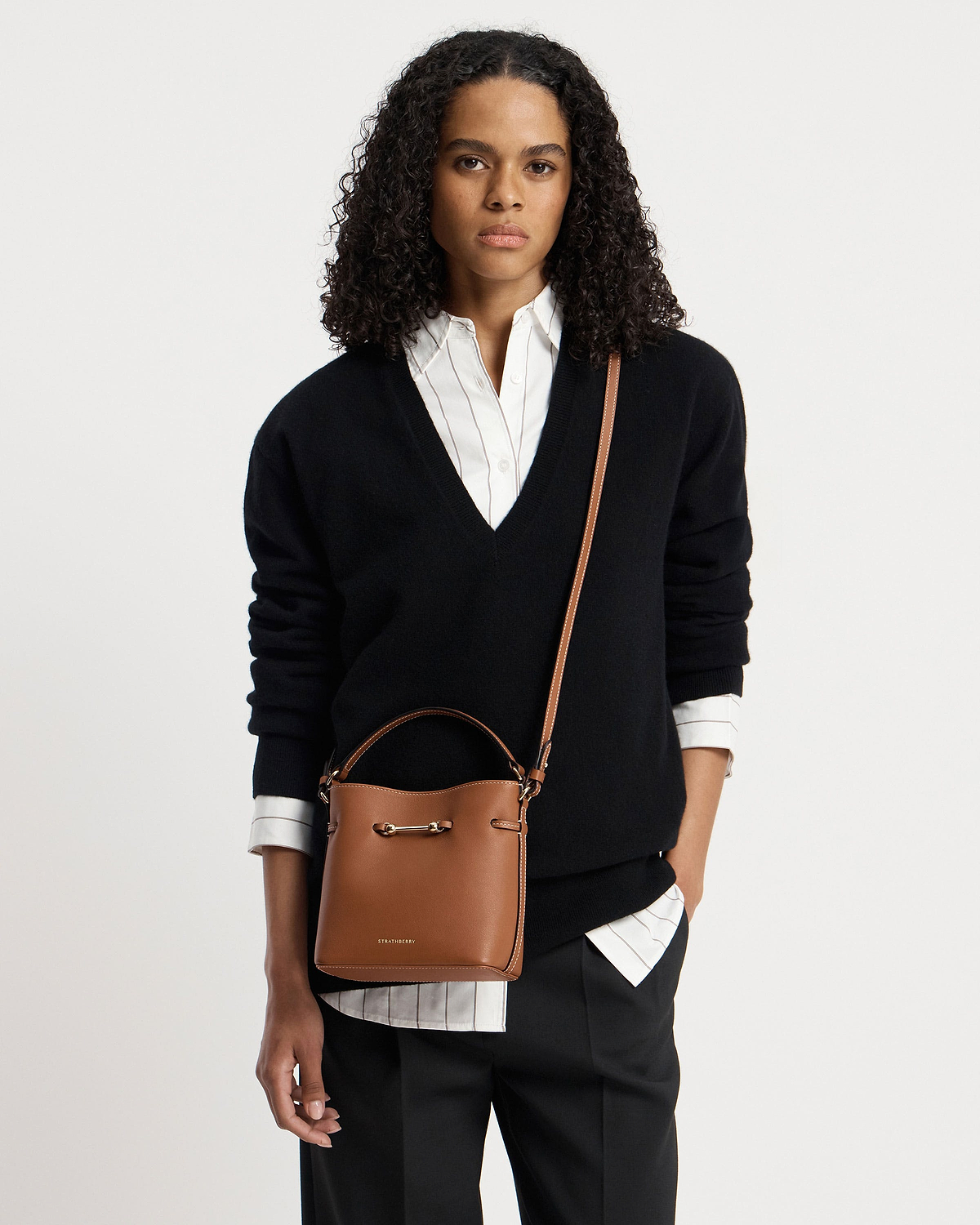 Woman wearing chestnut Corda Bucket Mini with visible Strathberry logo and crossbody strap.