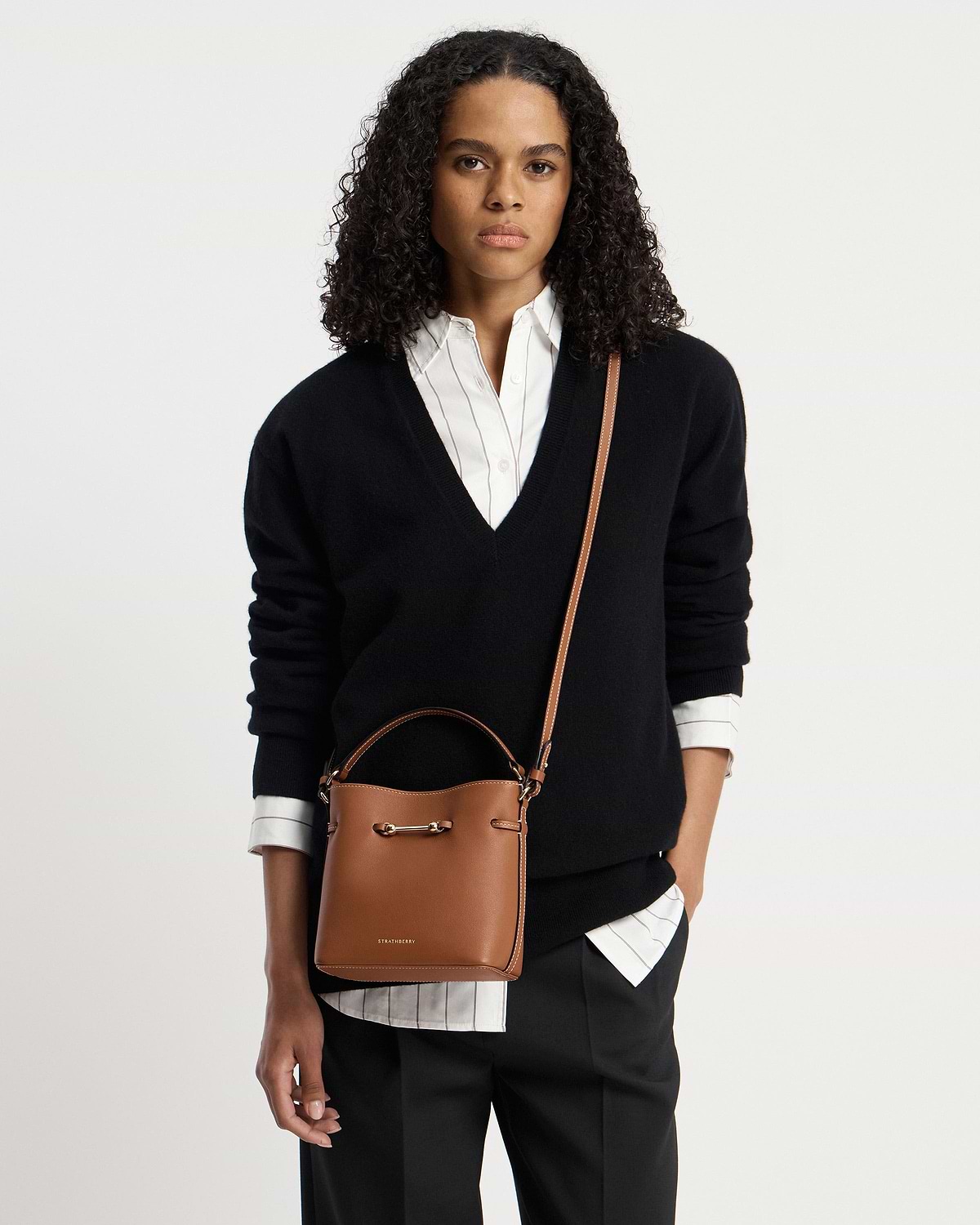 Woman wearing chestnut Corda Bucket Mini with visible Strathberry logo and crossbody strap.