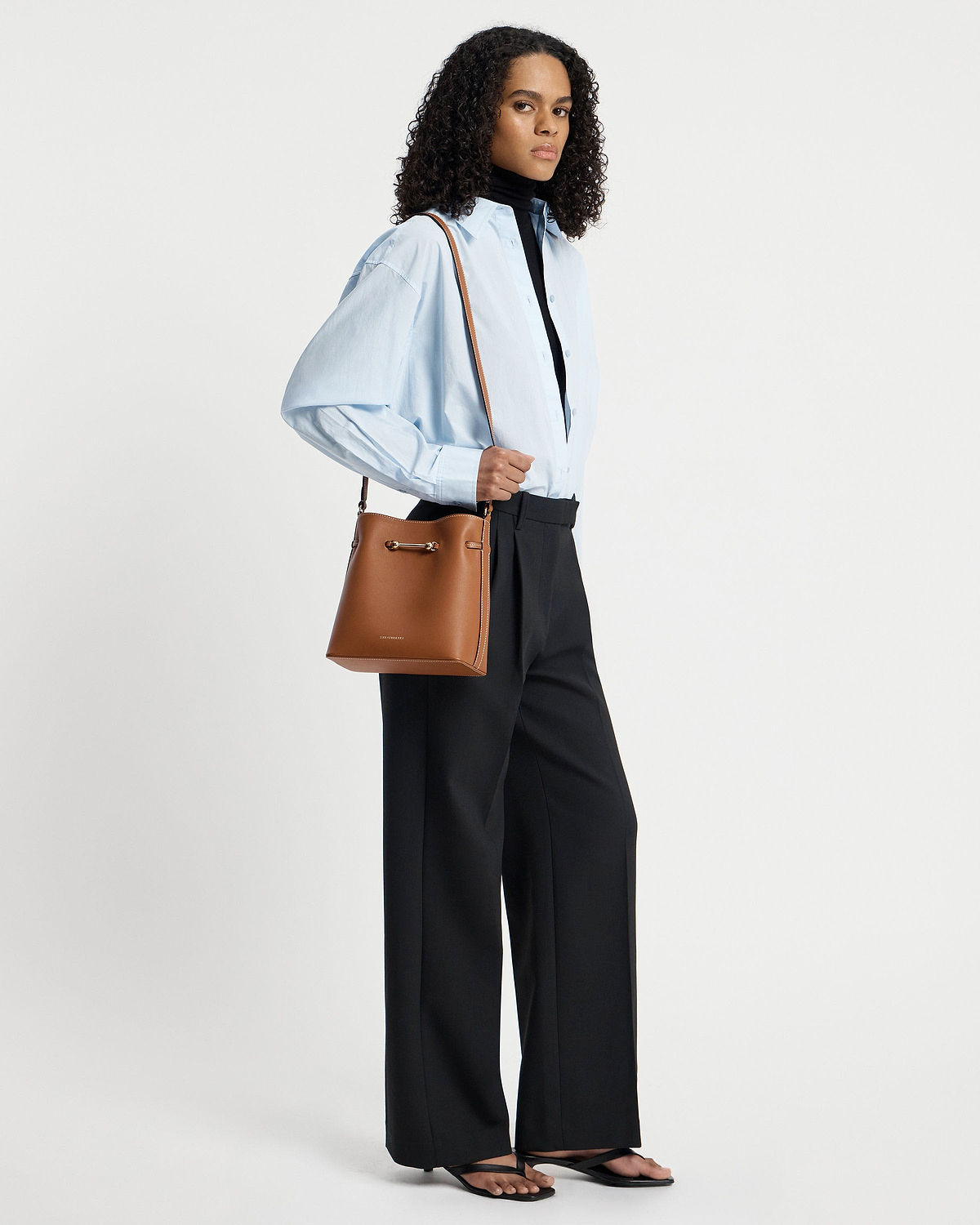 Model wearing chestnut Corda bucket bag over shoulder with light blue shirt.