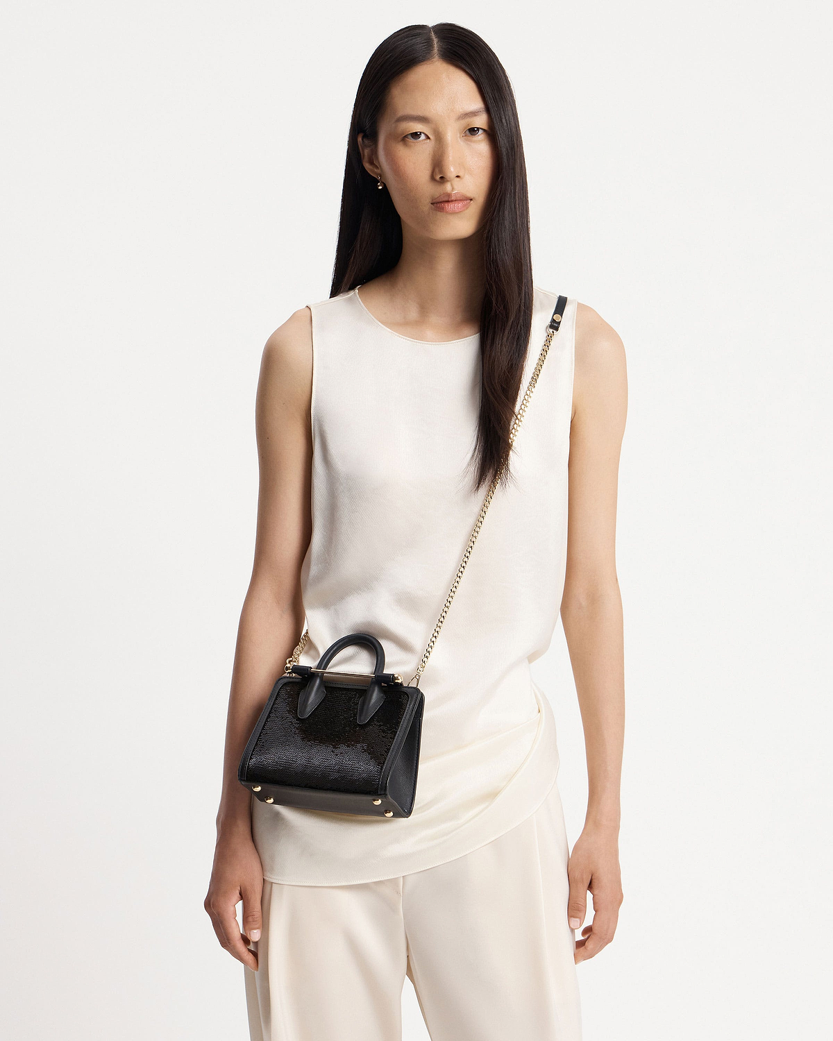 Model wearing black sequin nano tote with gold chain strap and handles.