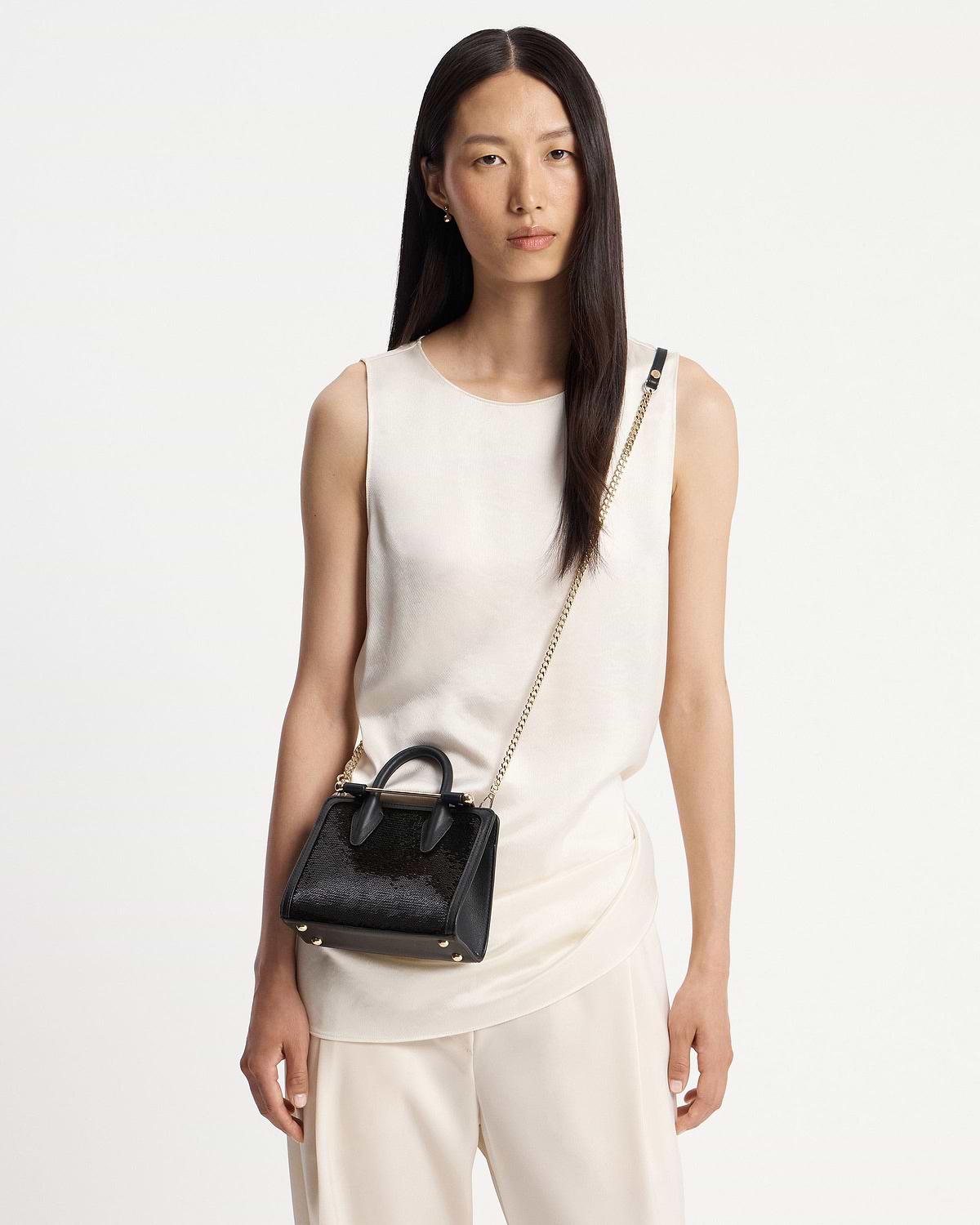 Model wearing black sequin nano tote with gold chain strap and handles.