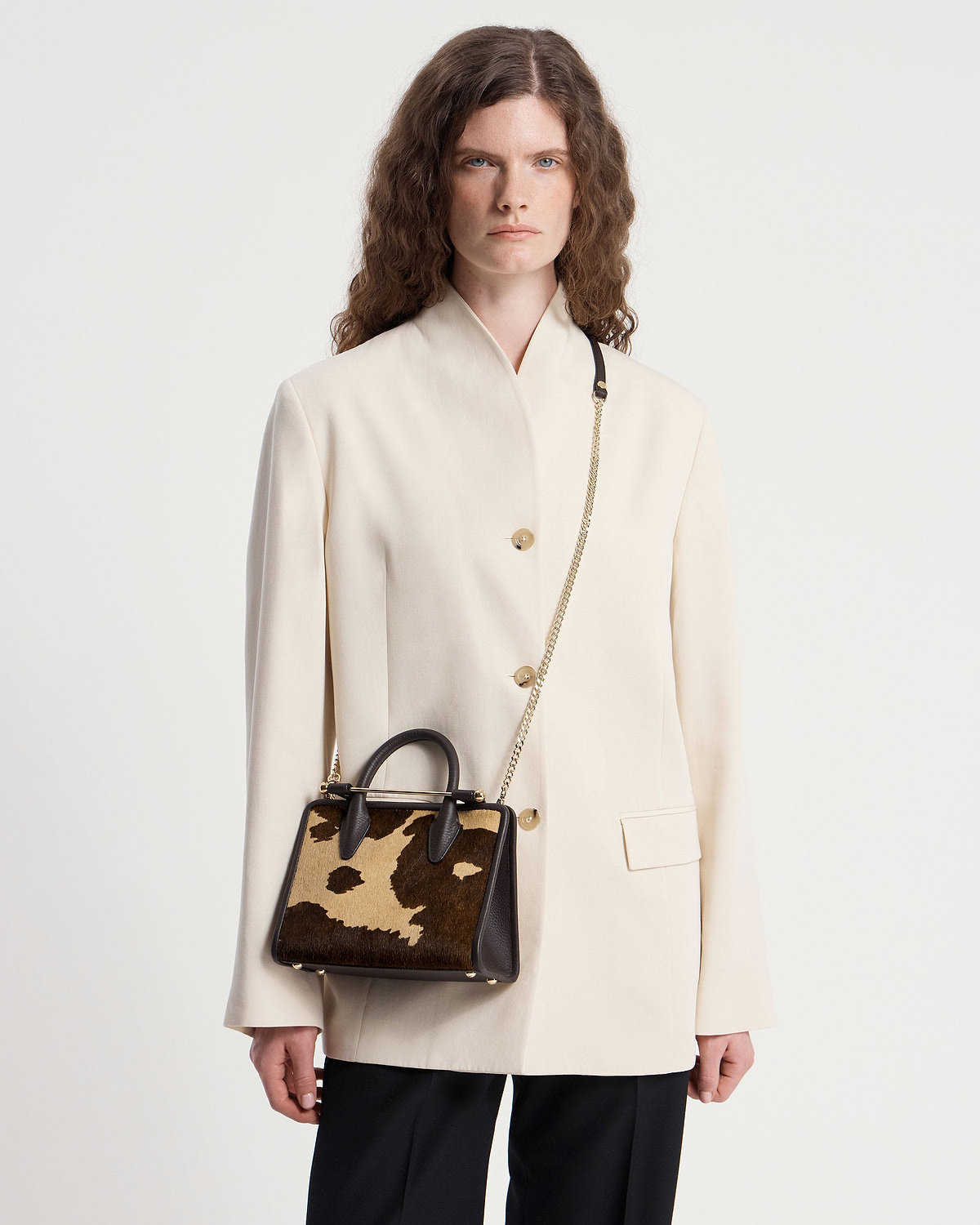 Model wearing cream blazer with mini tote in sand espresso spot print, gold chain strap.