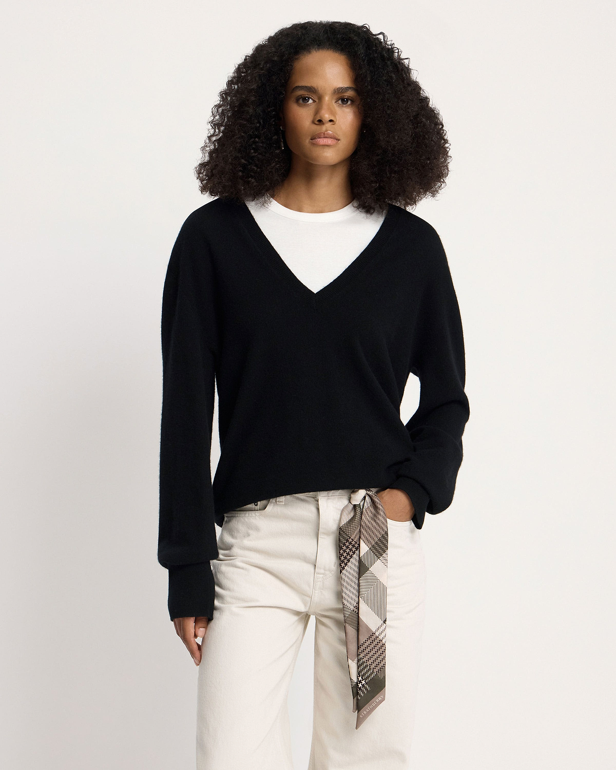 Model wearing a black V-neck sweater and white trousers with green tartan silk skinny scarf.