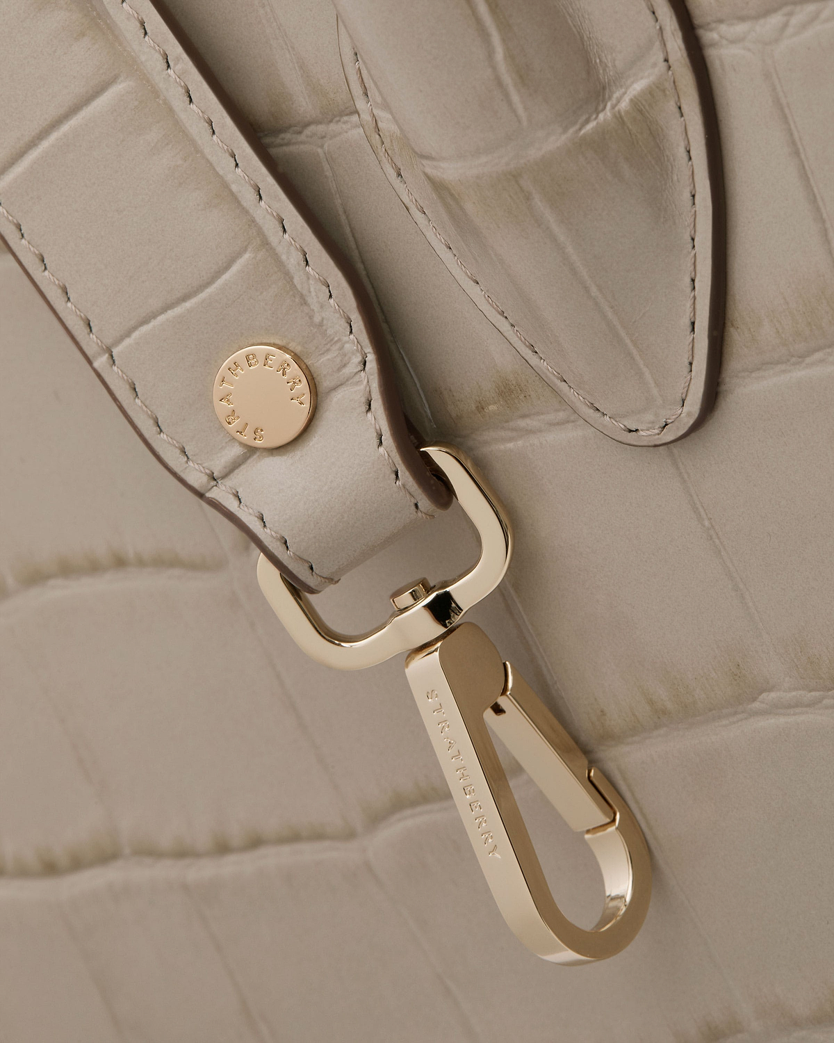 Close-up of croc-embossed midi tote strap with gold hardware engraved Strathberry