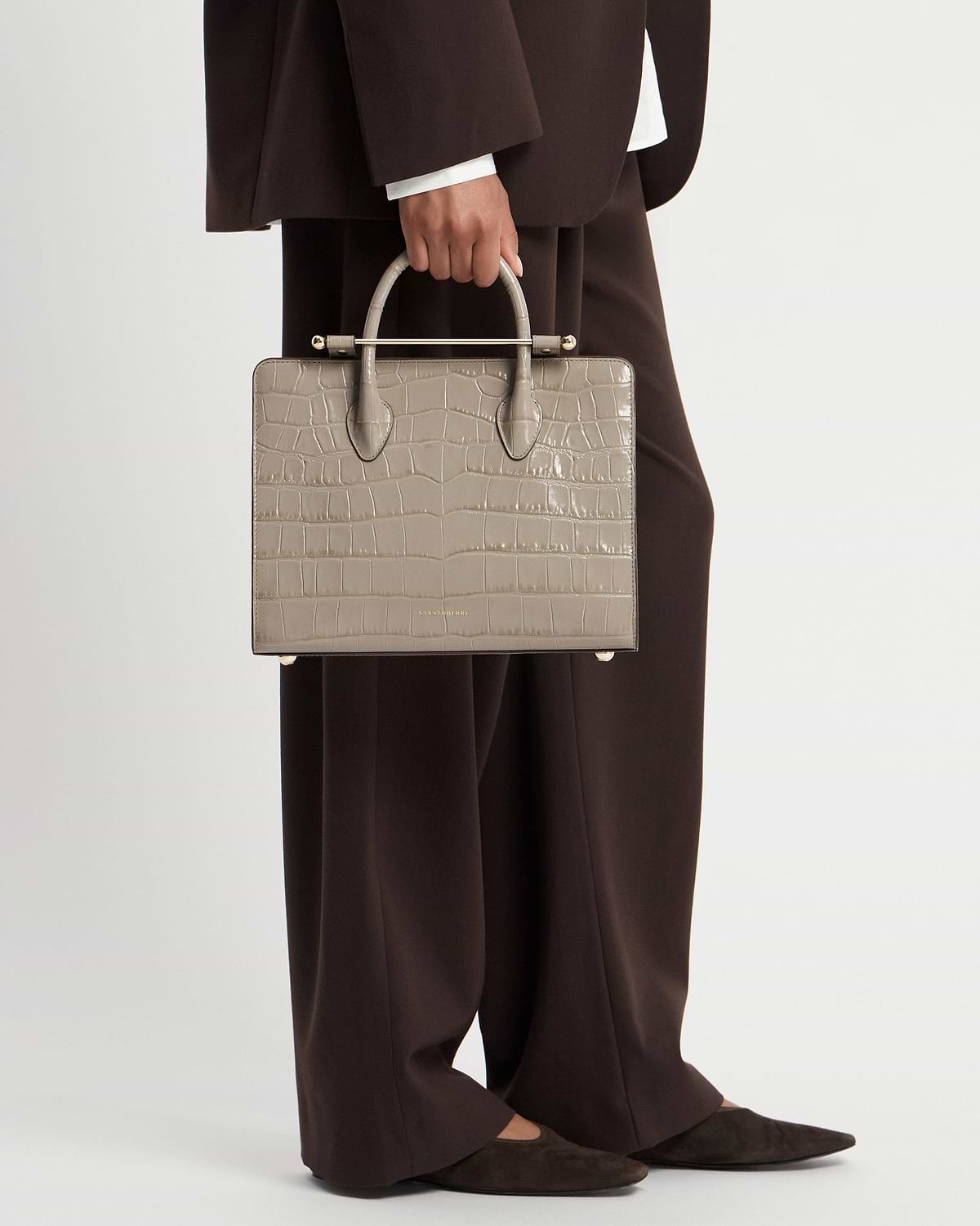 Model holding Strathberry croc-effect midi tote bag with top handles
