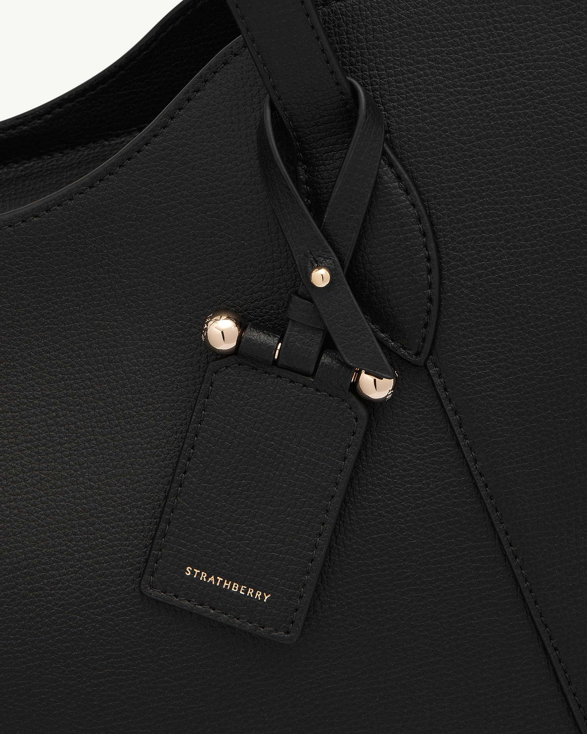 Black pebbled leather handbag strap and tag with gold studs and Strathberry logo