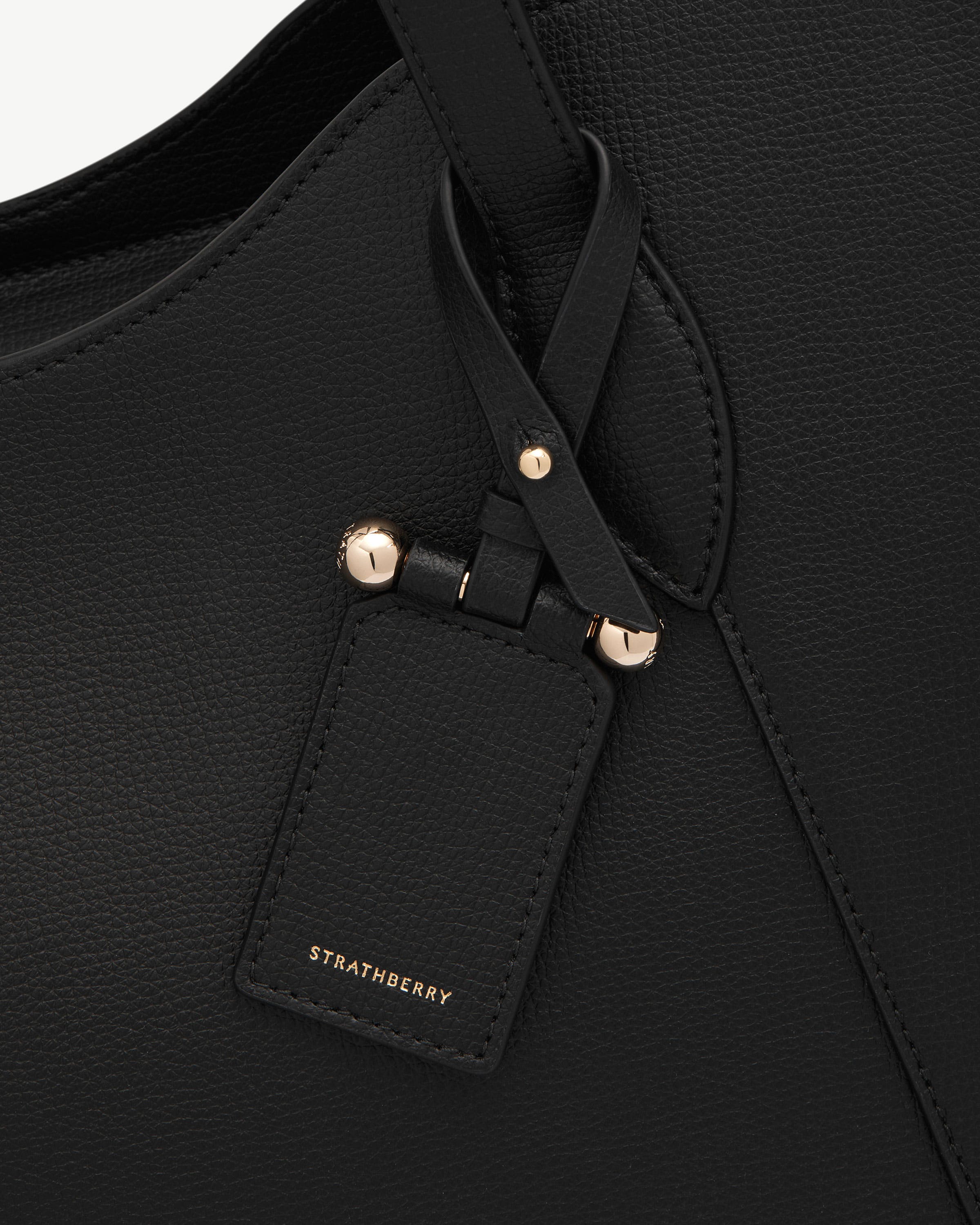 Black pebbled leather handbag strap and tag with gold studs and Strathberry logo