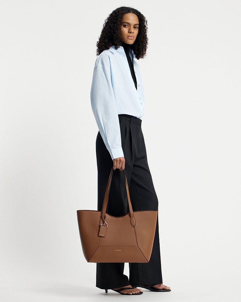 Model holding a hazelnut Strathberry Mosaic Cabas tote by the top handles.