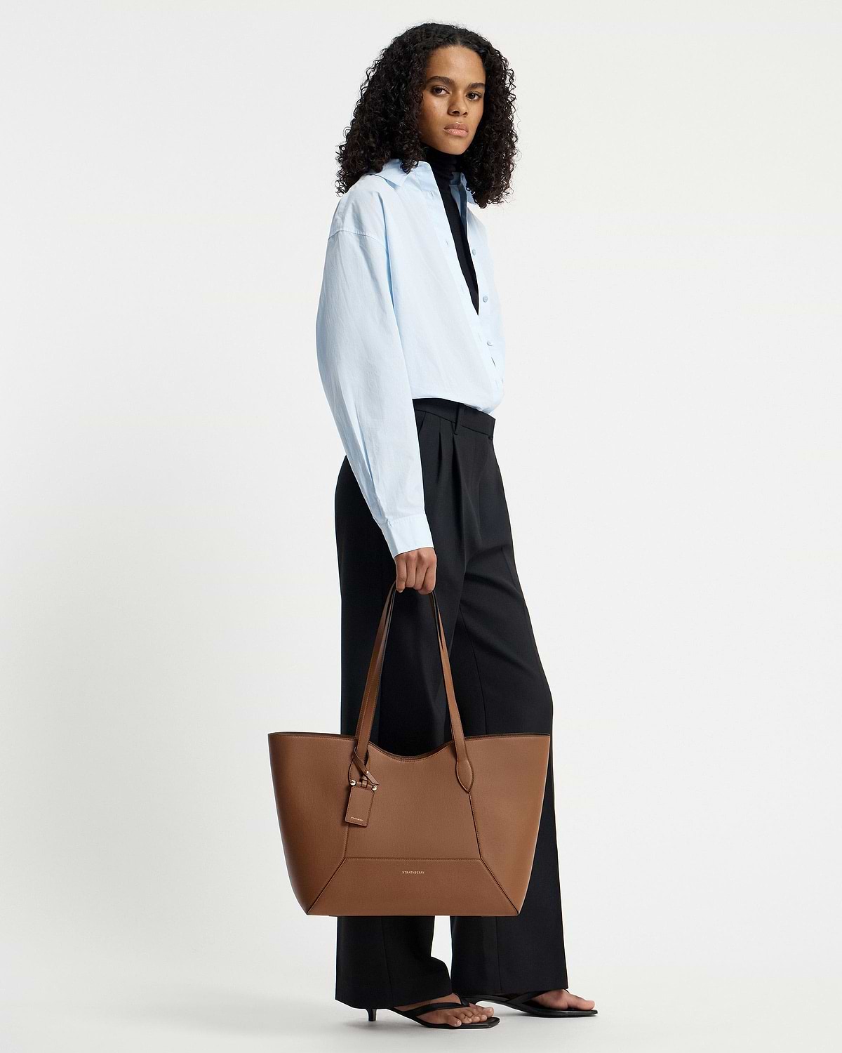 Model holding a hazelnut Strathberry Mosaic Cabas tote by the top handles.