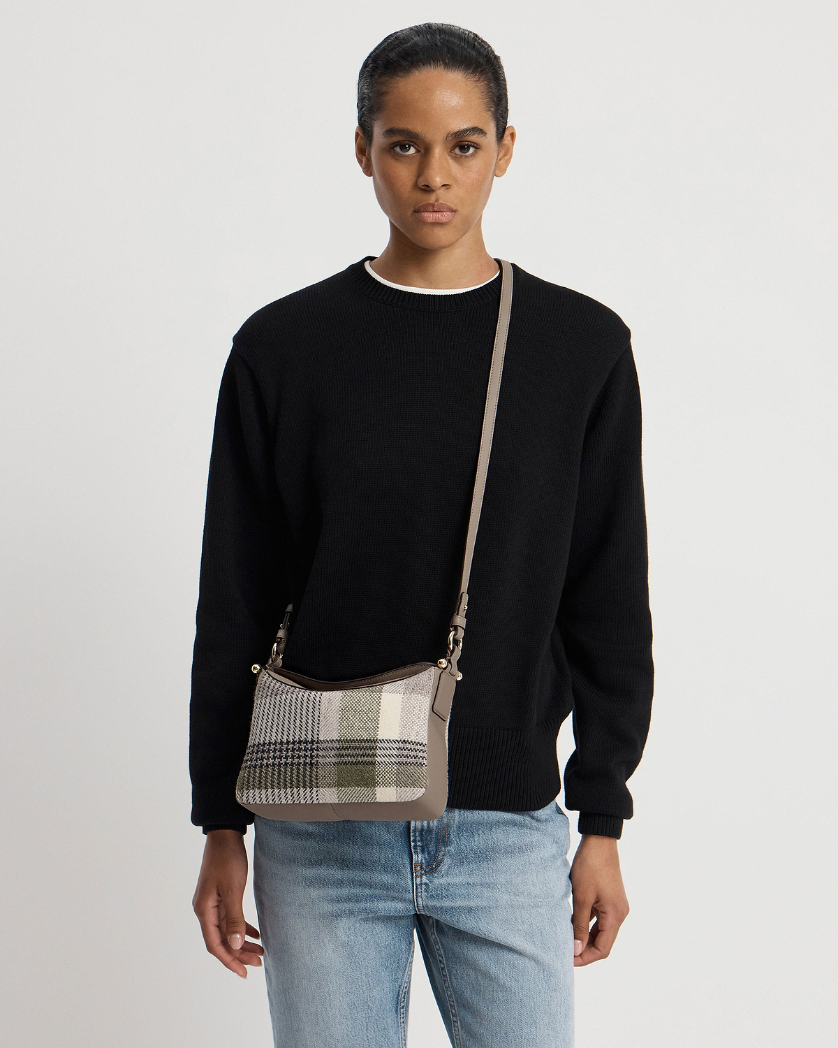 Model wearing black jumper and jeans with tartan taupe crossbody bag.