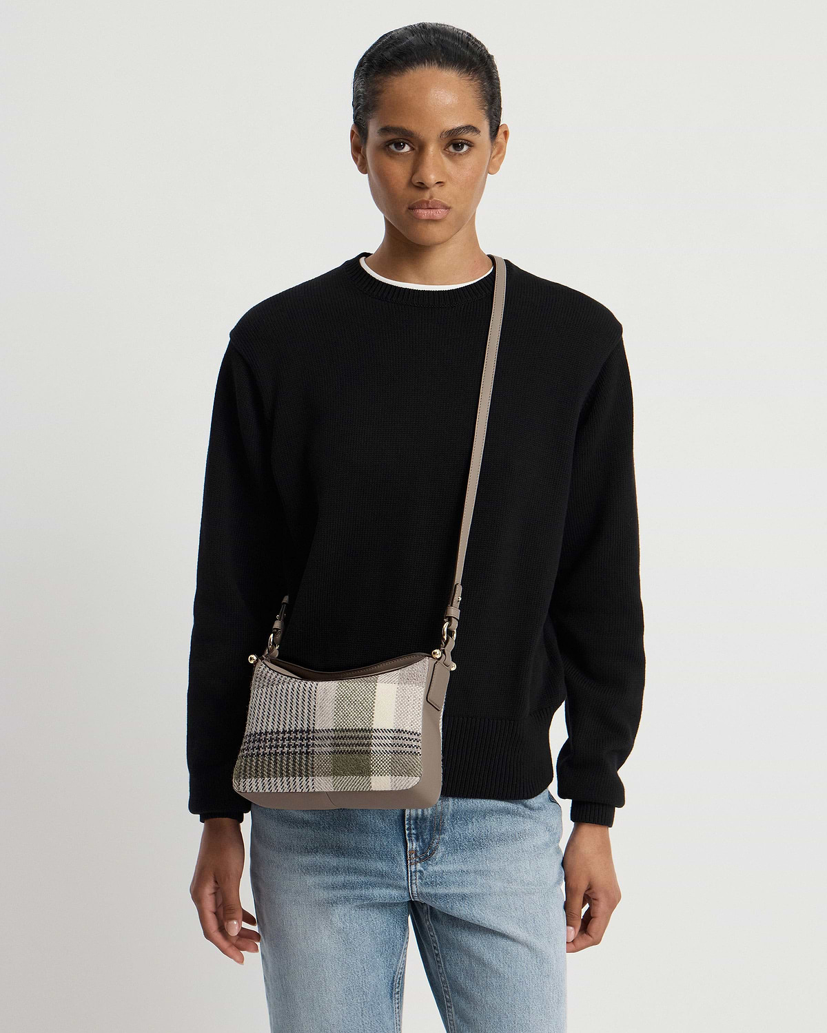 Model wearing black jumper and jeans with tartan taupe crossbody bag.