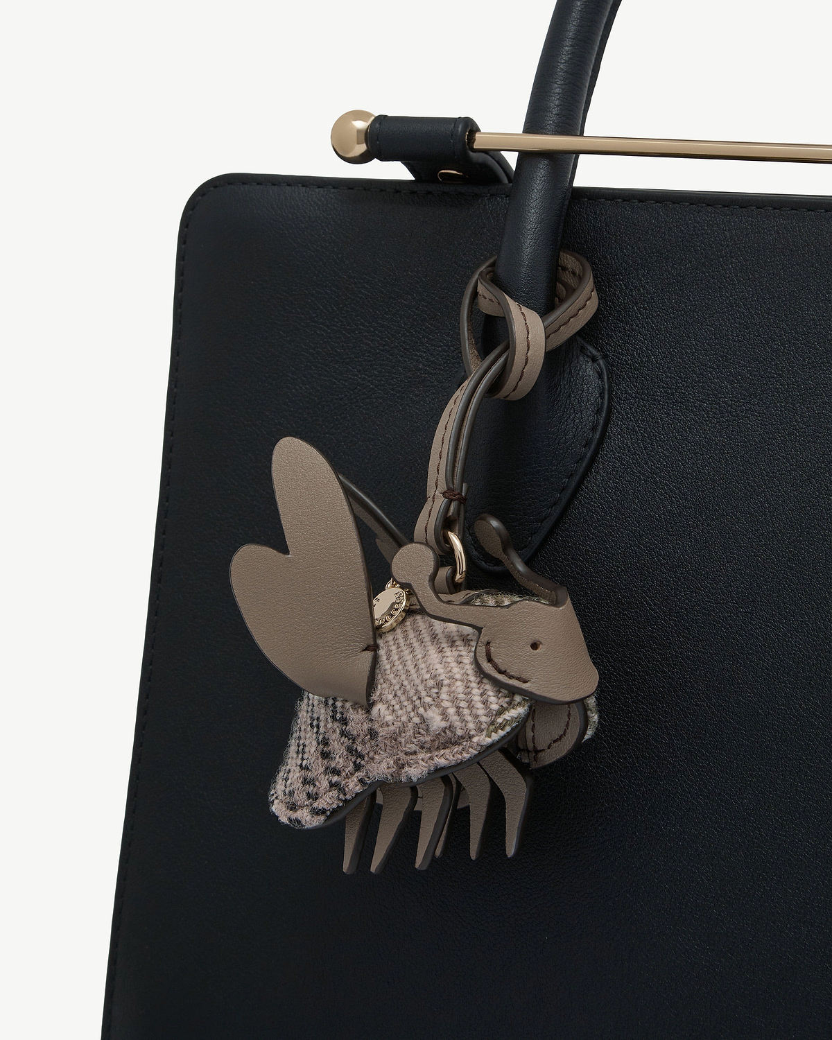Beige leather and tartan fabric bag charm attached to black leather bag handle.