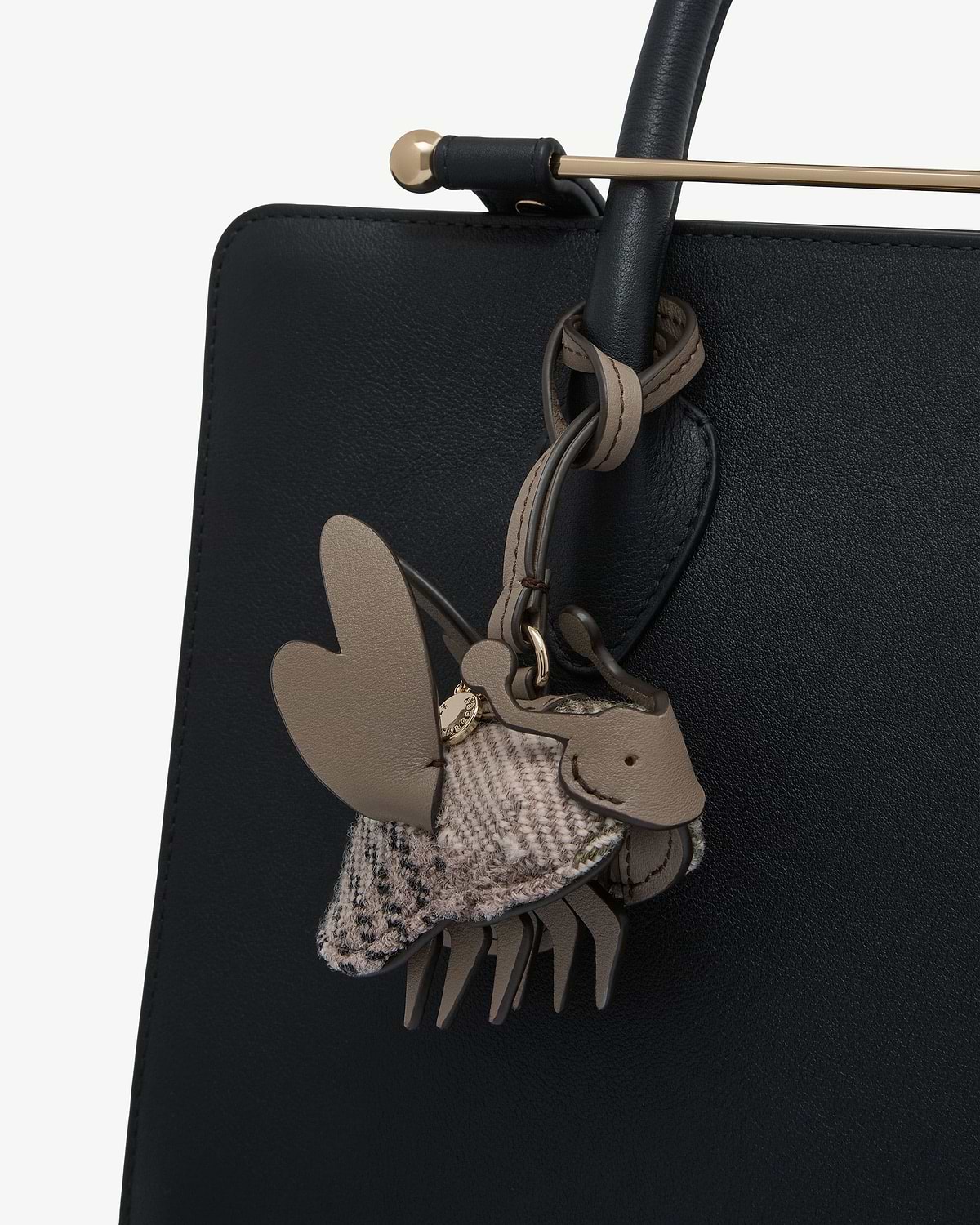Beige leather and tartan fabric bag charm attached to black leather bag handle.