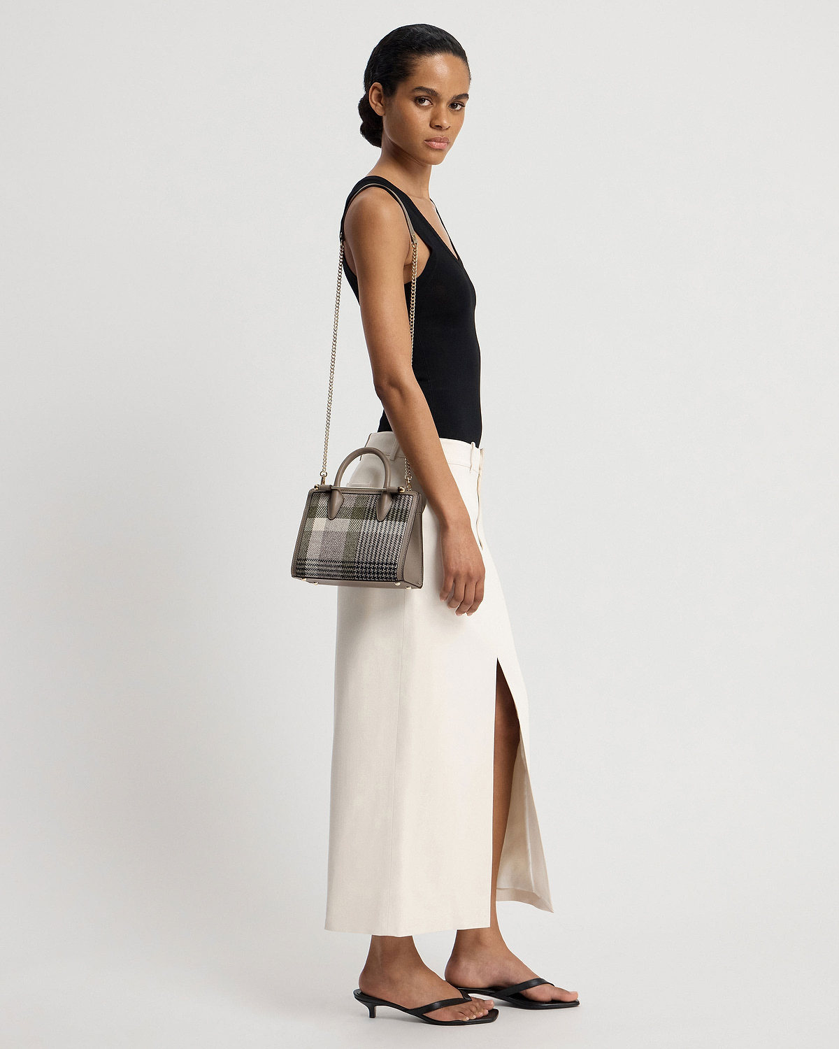 Model wearing black top and cream skirt carrying a tartan taupe mini tote.