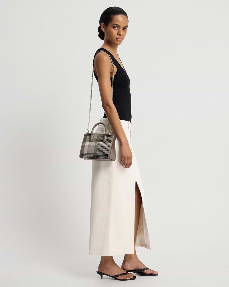 Model wearing black top and cream skirt carrying a tartan taupe mini tote.