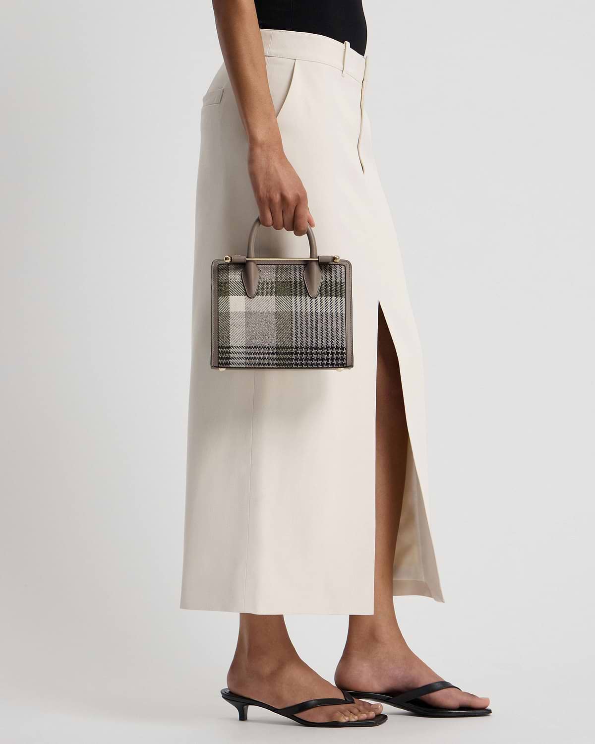 Model holding a taupe tartan mini tote by the top handle at their side