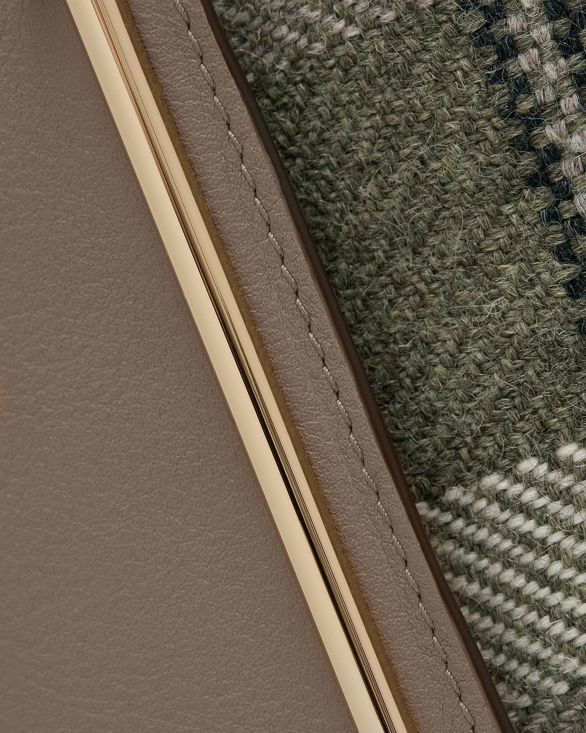 Taupe leather edge with gold metal trim beside green tartan woven fabric.