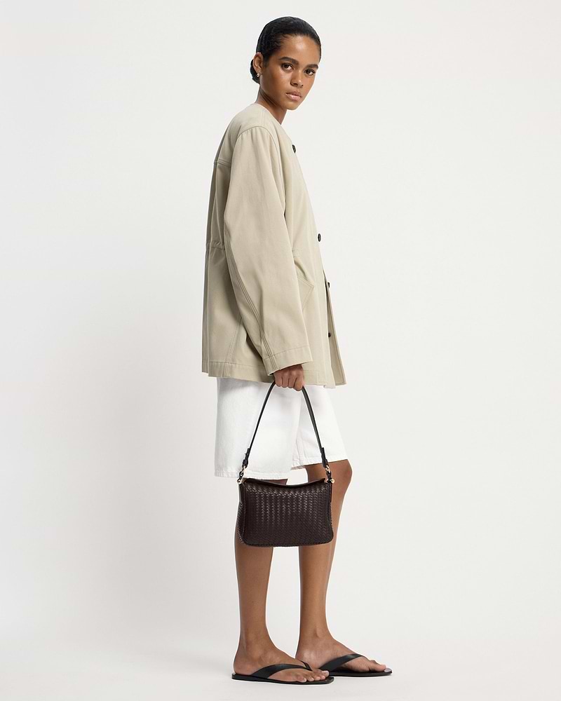 Model in beige jacket holding chocolate woven leather shoulder bag.