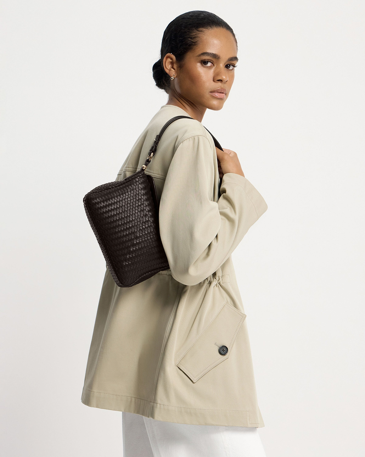 Woman wearing a chocolate woven leather shoulder bag, looking over her shoulder.