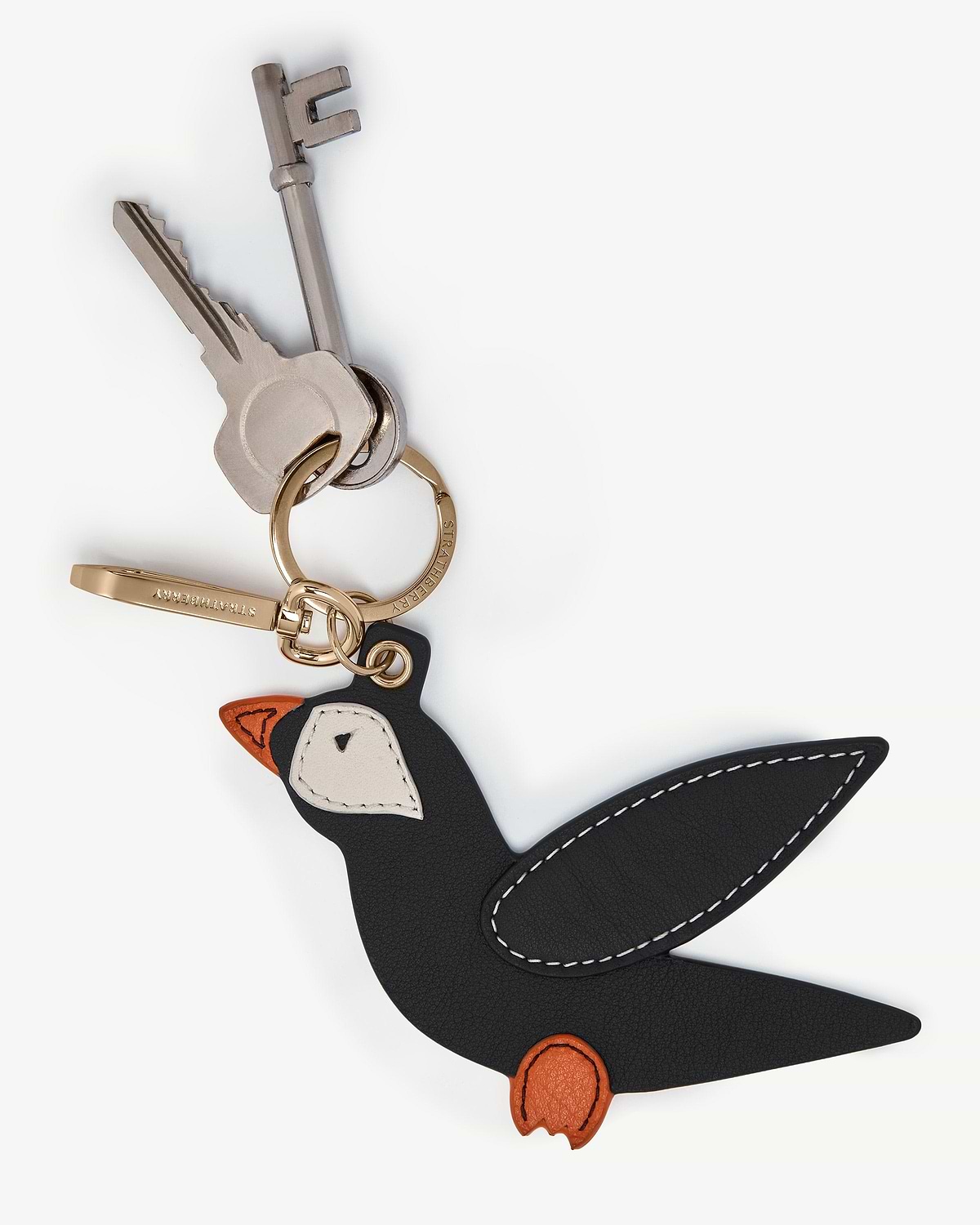 Strathberry black puffin bag charm with vanilla and marmalade details on gold keyring.