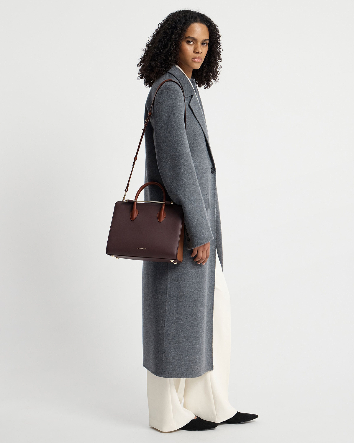 Model in grey long coat carrying Strathberry burgundy, walnut and chestnut midi tote.