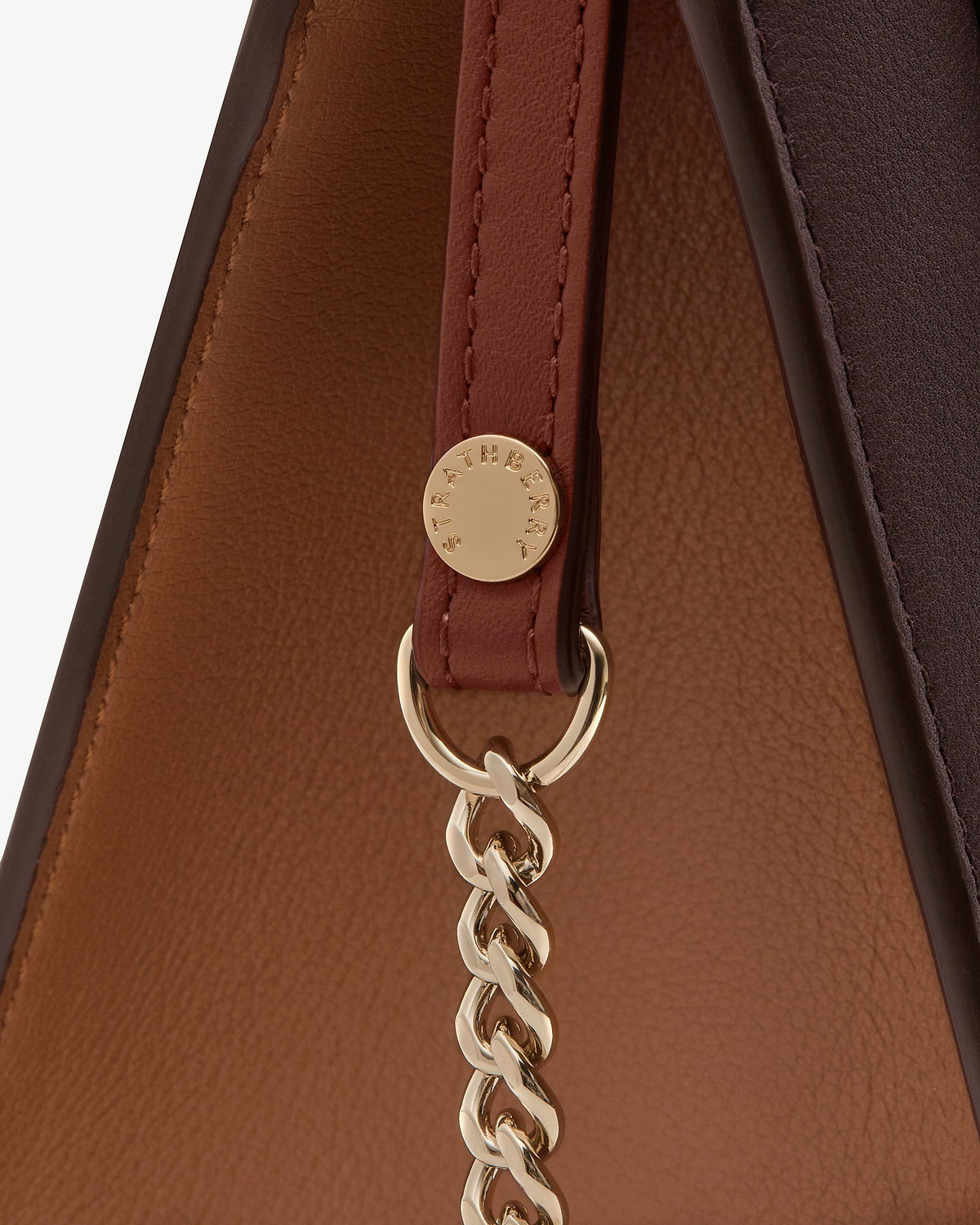 Close-up of burgundy mini tote strap and gold chain with Strathberry logo.