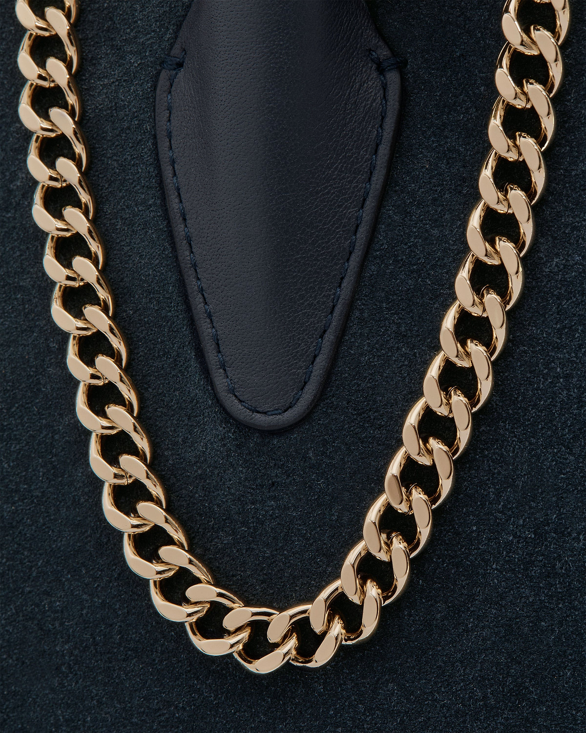 Navy suede mini tote showing gold chain strap and stitched leather tab.